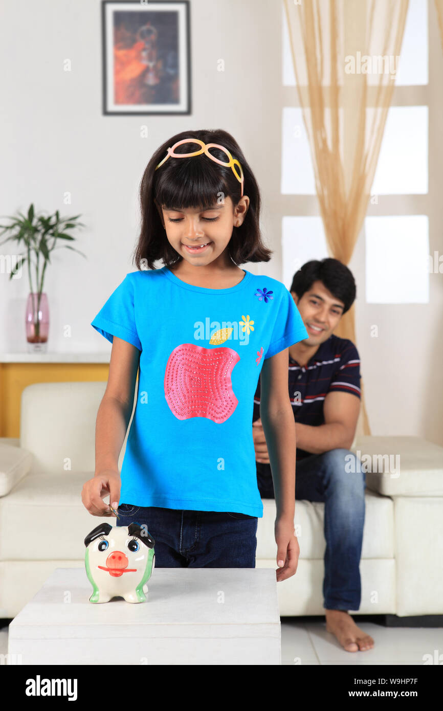 Girl putting coin into a piggy bank Stock Photo - Alamy