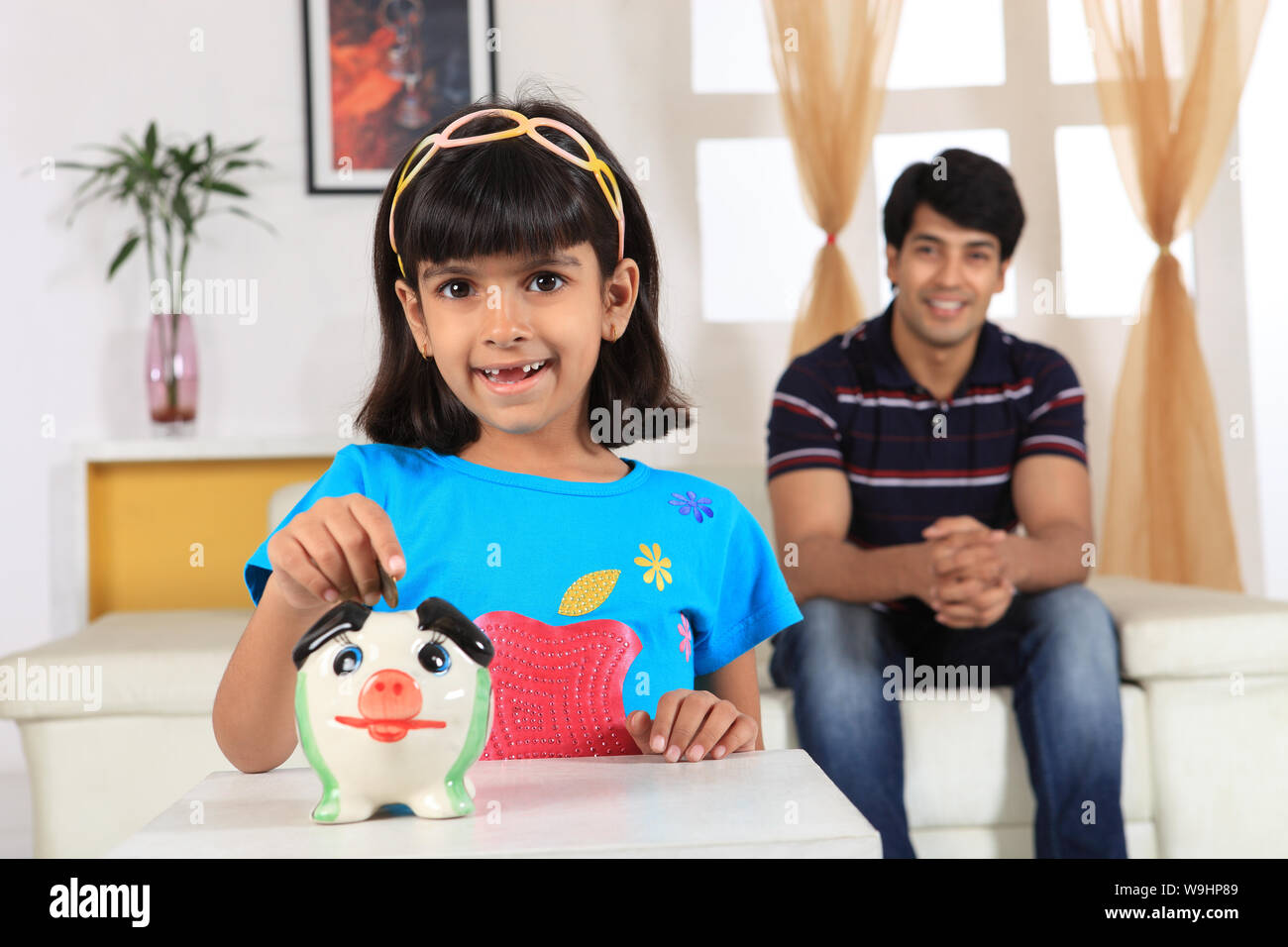 Girl putting coin into a piggy bank Stock Photo - Alamy