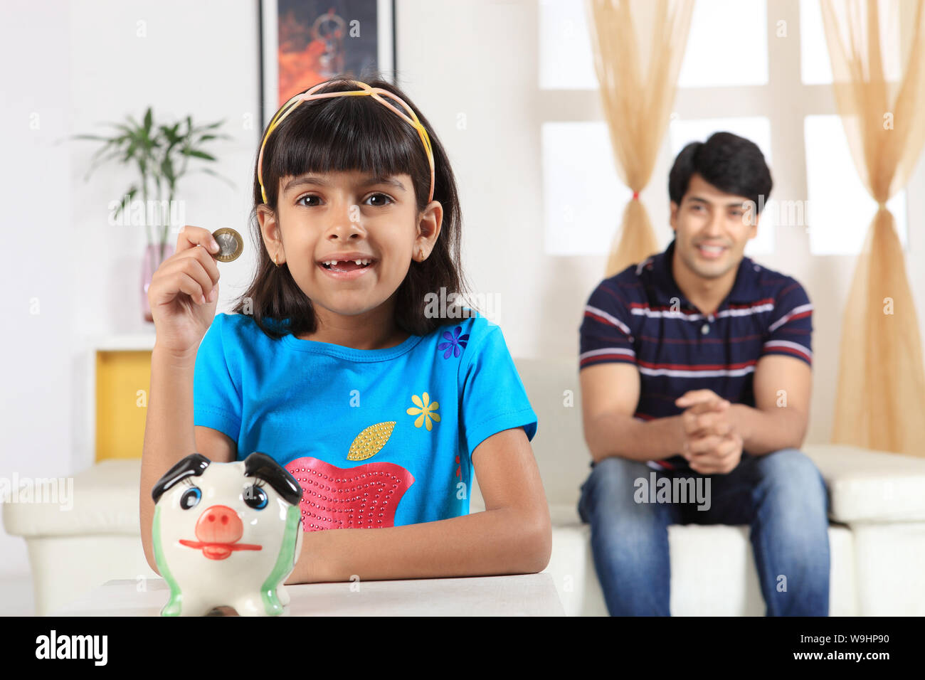 Girl putting coin into a piggy bank Stock Photo - Alamy