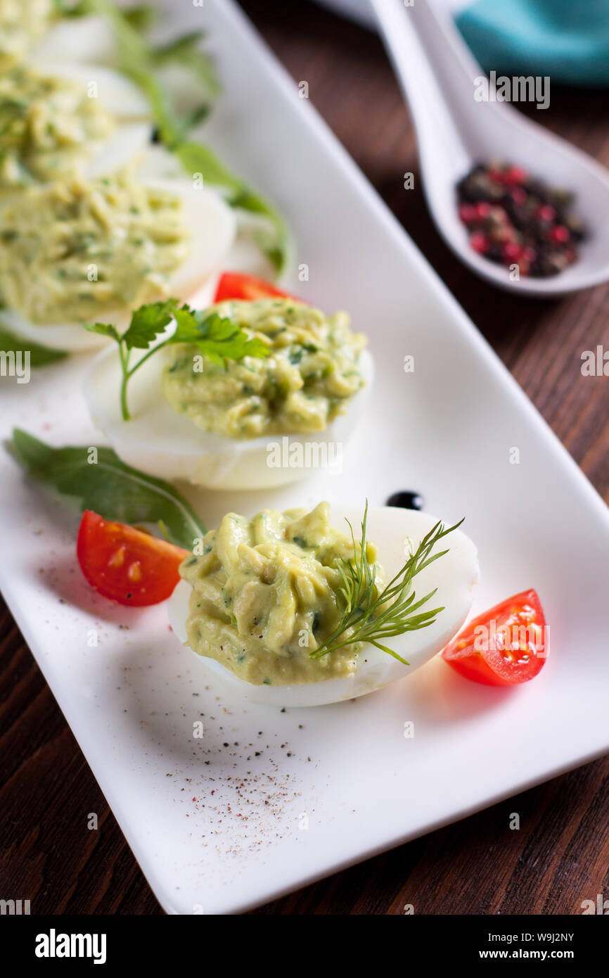 Deviled eggs with avocado puree and spices decorated with herbs and cherry tomatoes Stock Photo