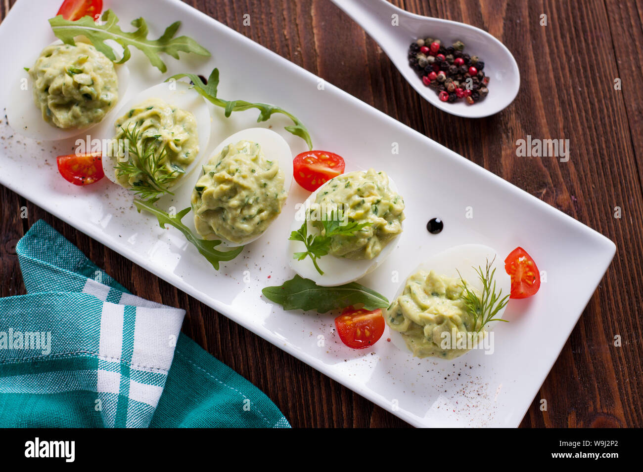 Deviled eggs with avocado puree and spices decorated with herbs and cherry tomatoes Stock Photo
