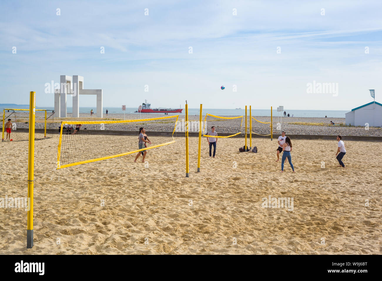 A group playing a game of beach volleyball at Sainte Adresse, Le Havre, Normandy, France as a tanker sails past Stock Photo