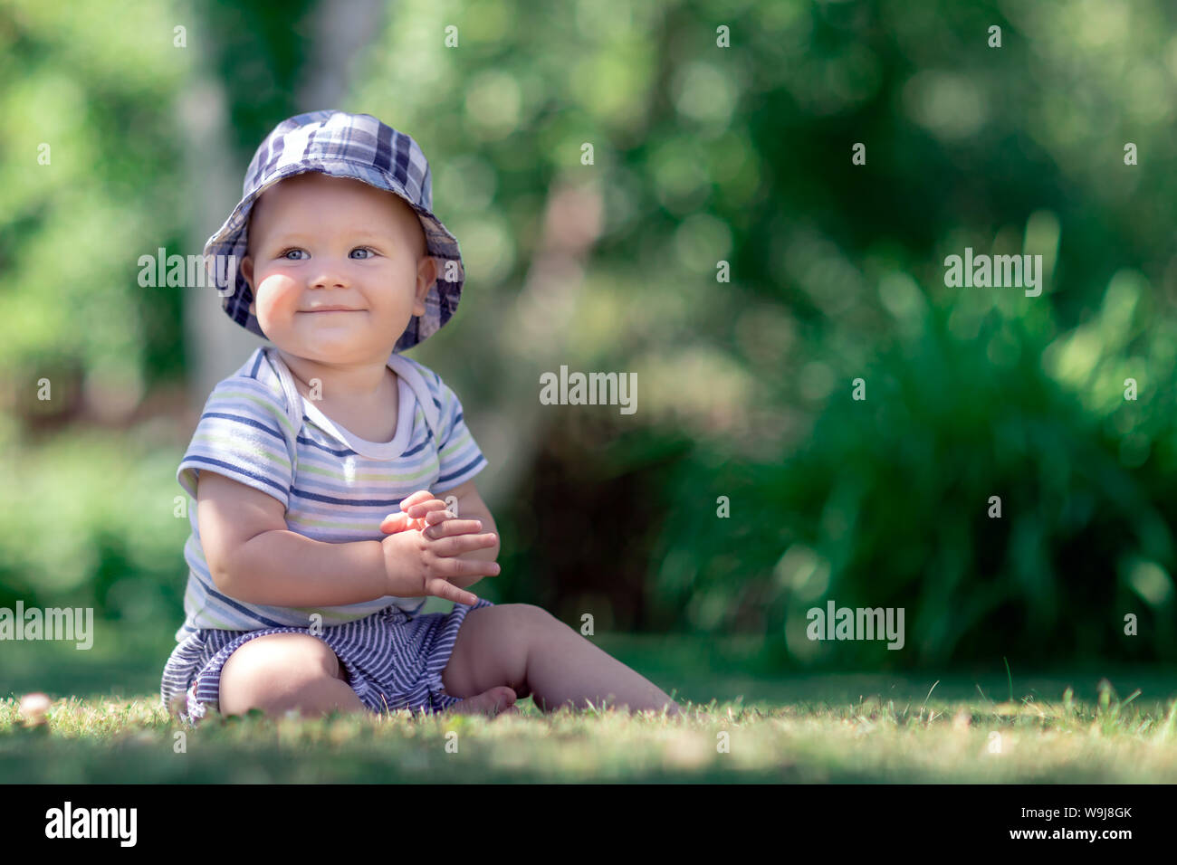 Cute baby sitting on the grass in the garden and applaud Stock Photo