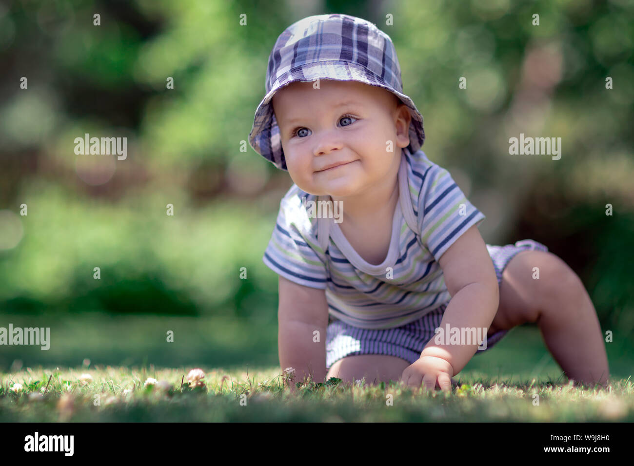 Baby with nice blue cap crawling on the green grass in the garden Stock Photo