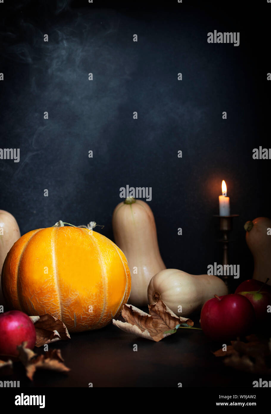 Pumpkins, apples, dry leaves on a table with candles and smoke ...