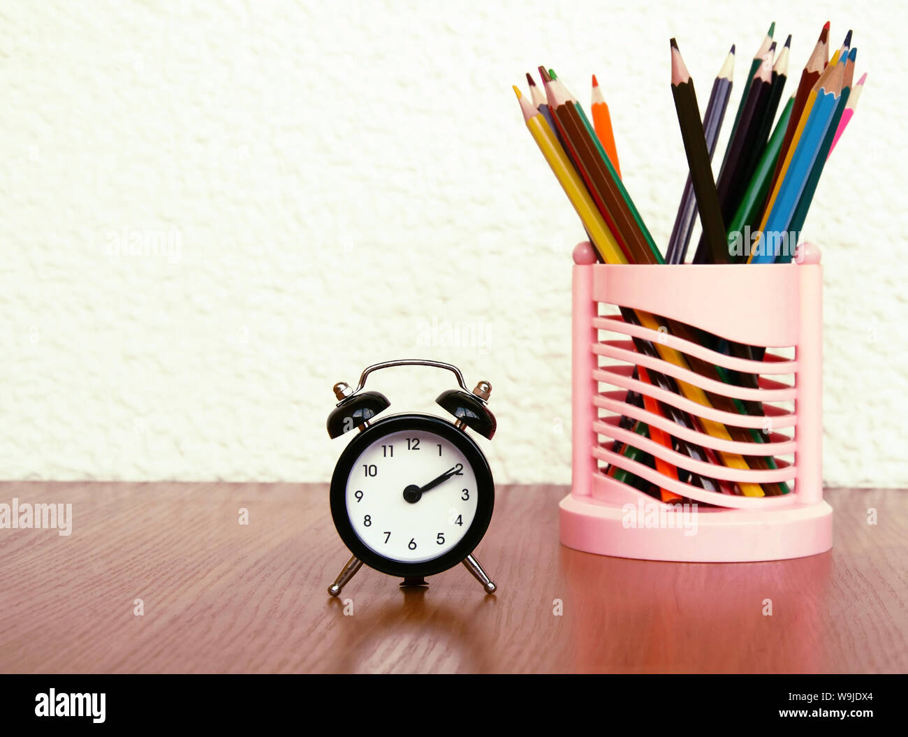 black alarm clock with arrows and color pencils on a wooden table, close-up Stock Photo