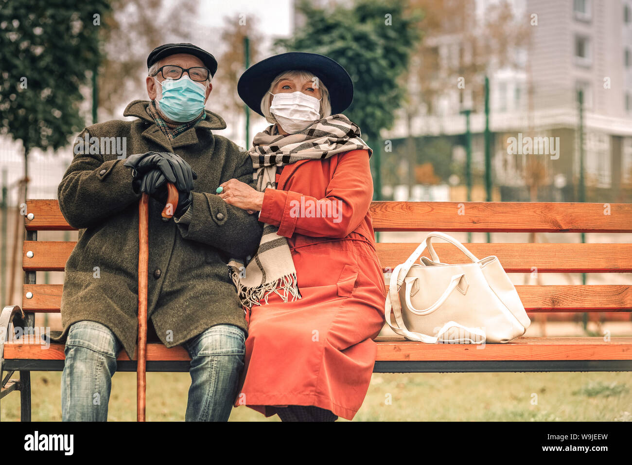 Ill senior couple with face masks relaxing on bench in park Stock Photo ...