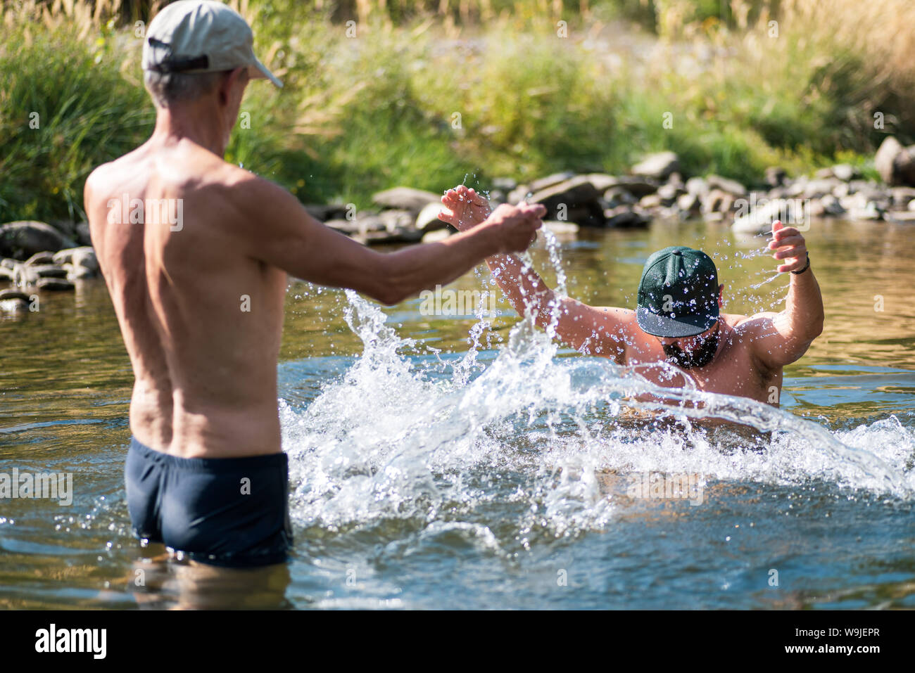 Father and son splashing each other with water in the river, summer fun Stock Photo