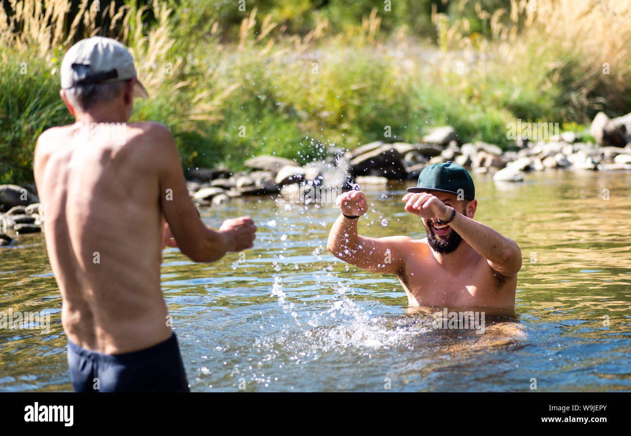 Father and son splashing each other with water in the river, summer fun Stock Photo