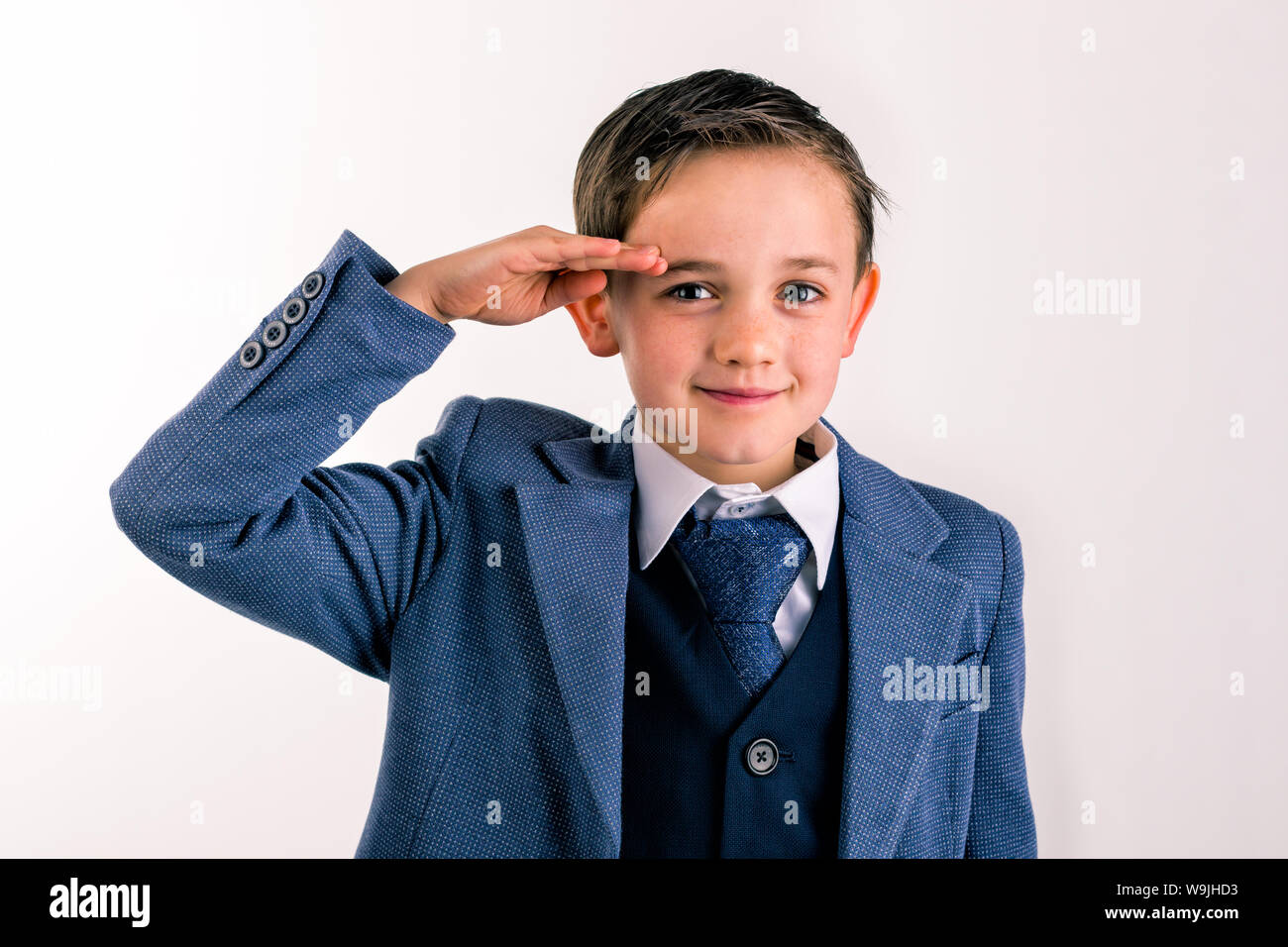 closeup portrait of 8 year old boy dressed in a suit saluting Stock