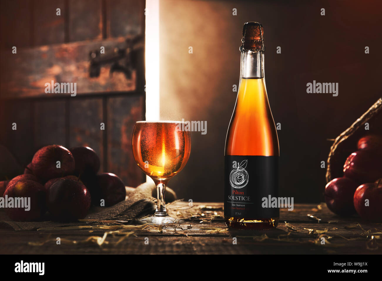 Pilton Solstice Cider on wooden table with a barn door open behind and light coming through. Stock Photo