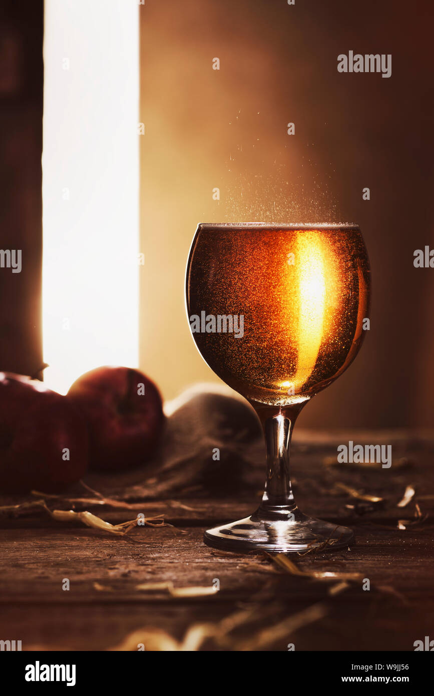 Full glass of golden cider on a rustic wooden table with the late evening sun coming through a gap in a door. Stock Photo