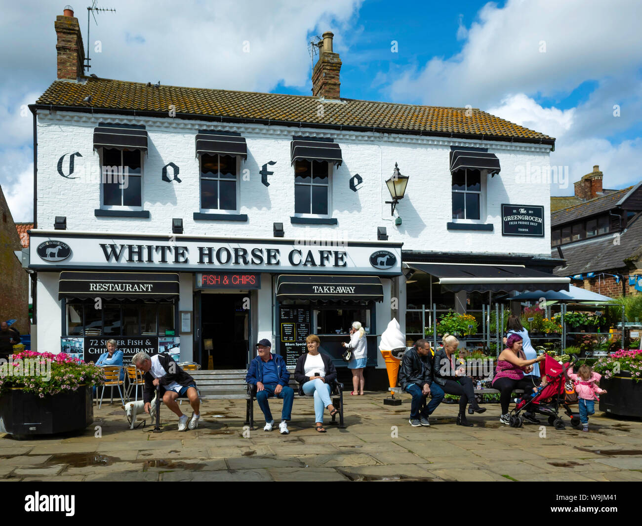 People relaxing outside the White Horse Café and fish and chip shop in Thirsk Market Place in the town centre on a warm summer day Stock Photo