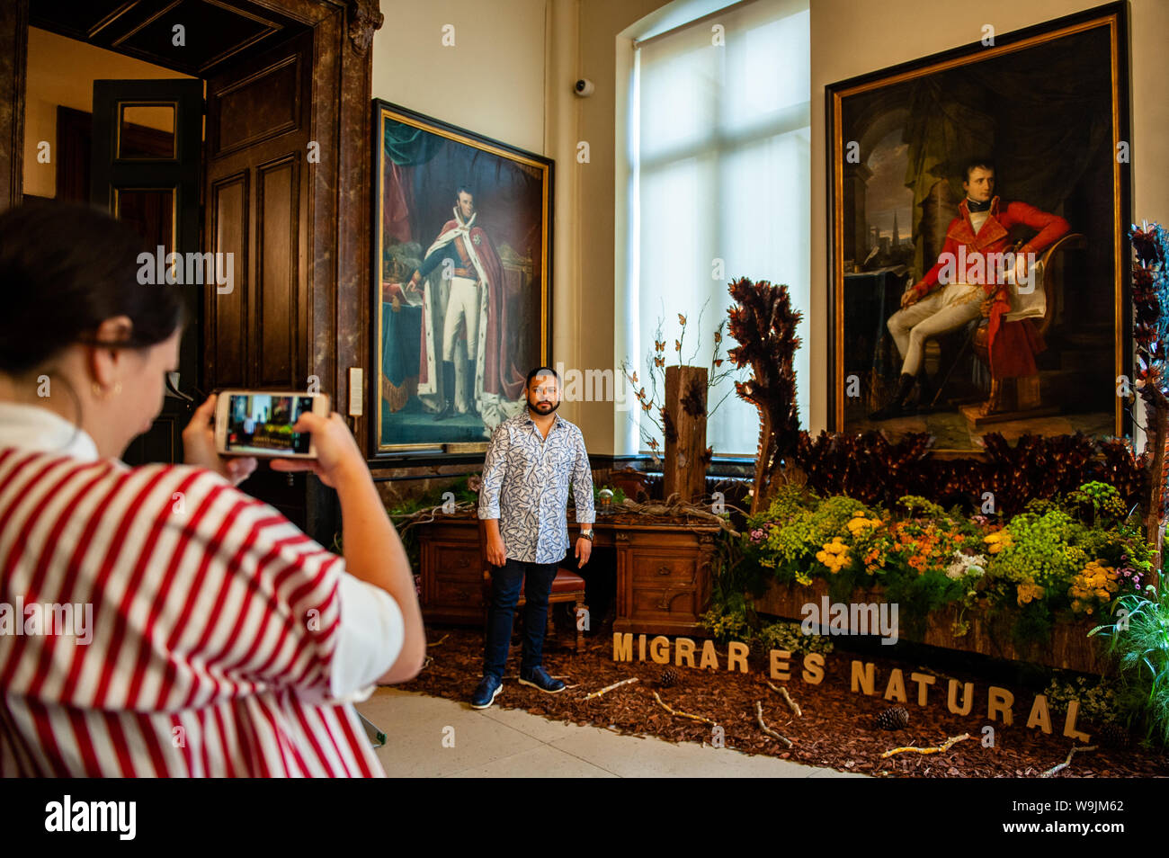 A woman takes a photo of one of the Mexican artists with his floral art during the occasion.Flower time is a biennial initiative that was launched in 2013 by the City of Brussels and the ASBL (non-profit organization) Tapis de Fleurs de Bruxelles. Under the theme 'A World of Floral Emotions', more than 30 top florists from 13 countries decorated the magnificent rooms of Brussels City Hall, a Unesco masterpiece of Gothic architecture. Brussels’ famous Grand Place hosted for the occasion a stunning flower arch composed of 500 fuchsias. This year, the artistic direction is once again in the hands Stock Photo