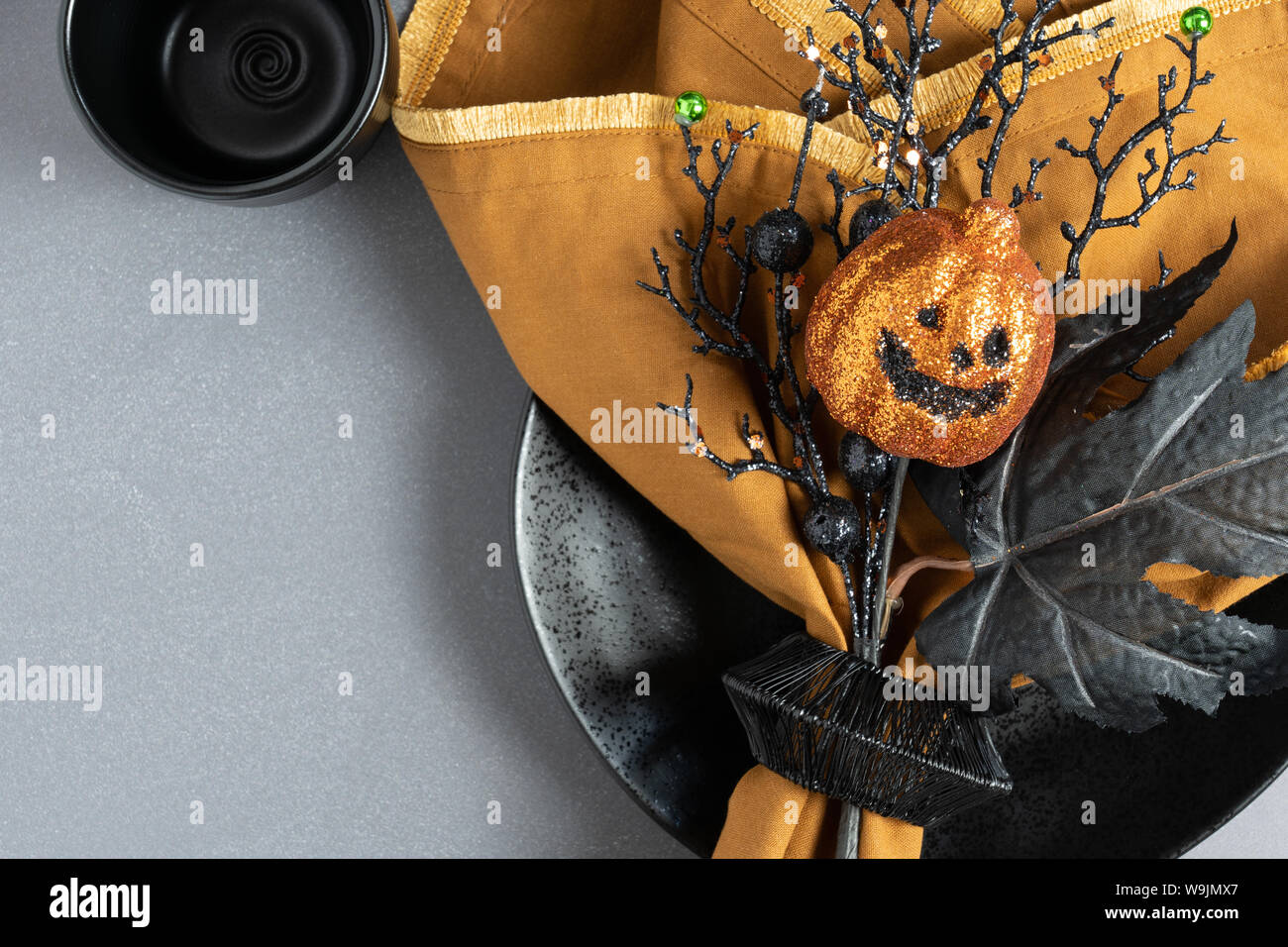 Orange and black place setting with napkin, plate, pumpkin, leaf, and twigs on a dark background with room for text Stock Photo