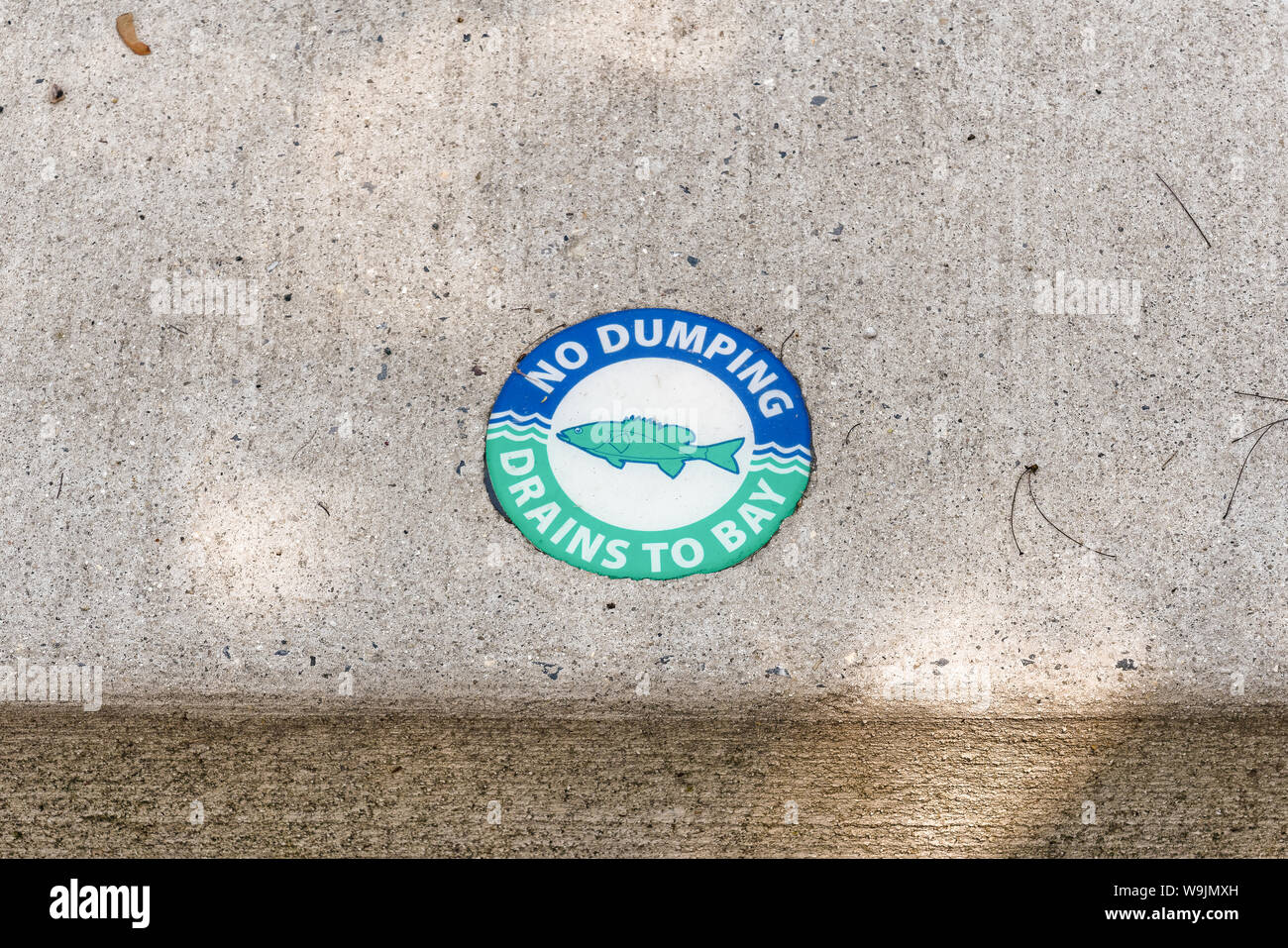 Chesapeake City, MD - May 19, 2019: Sidewalk curb above storm sewer drain with blue and green medallion with a fish on it and the words 'No Dumping Dr Stock Photo