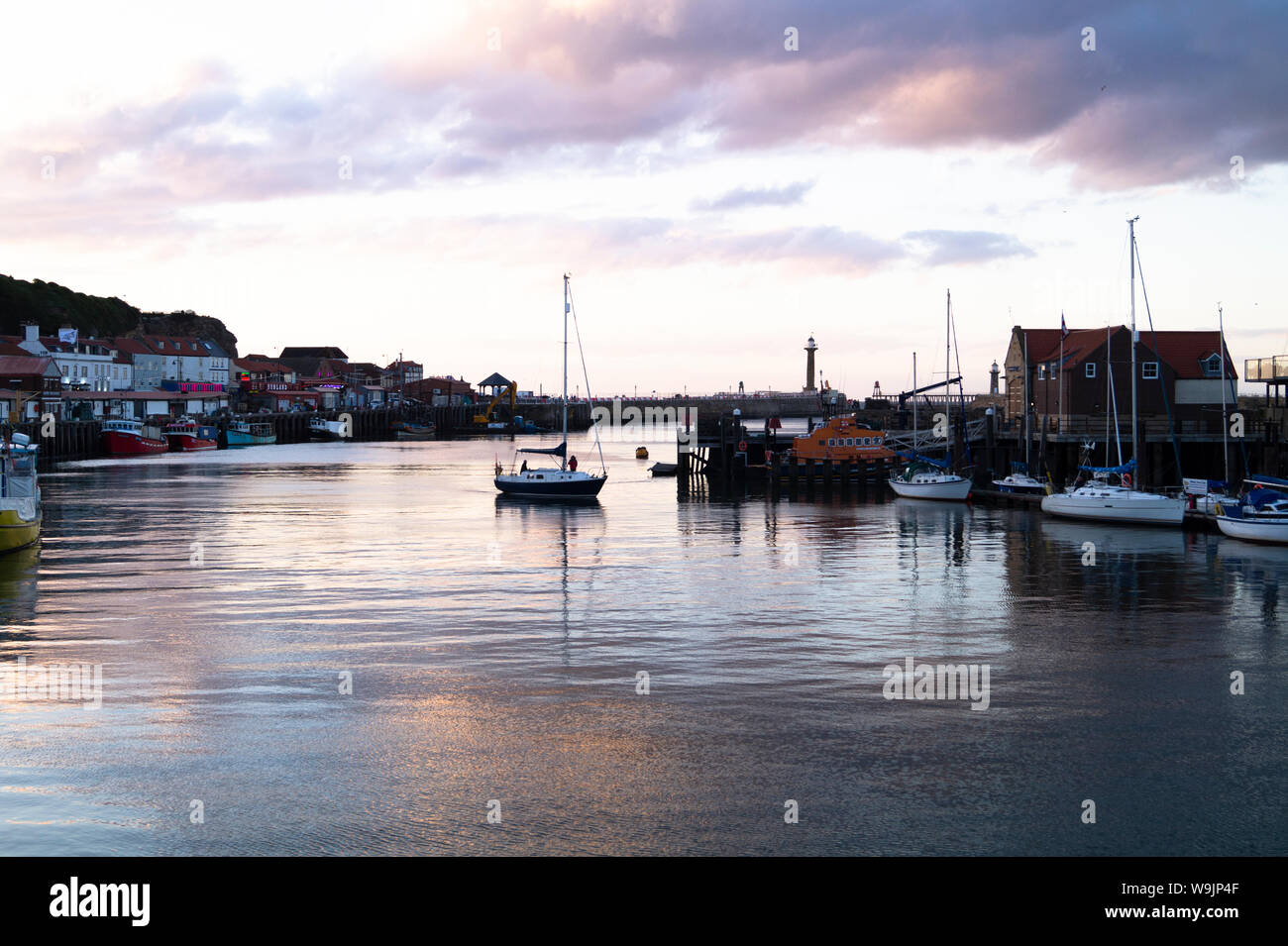 A Sailing boat finds it’s mooring at the end of the day in Whitby Harbour. Stock Photo