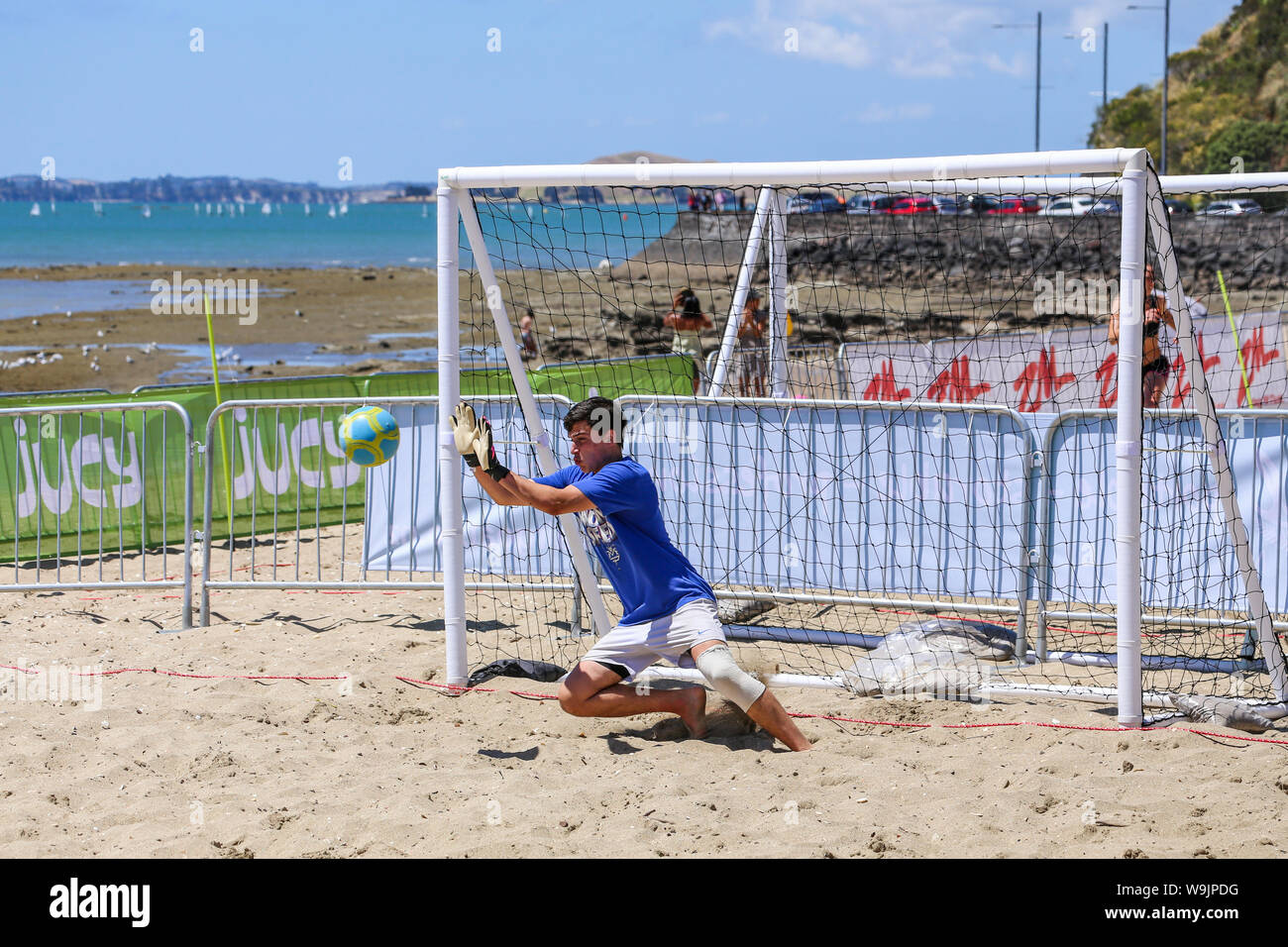A young man making a save in a game of beach volleyball against a back drop of boats and yachts on the ocean in Misson Bay. Stock Photo
