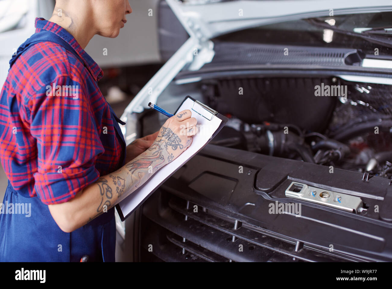 Automechanic with nice tattooes makes a list of problems needed to be checked before she finishes the repair. Stock Photo