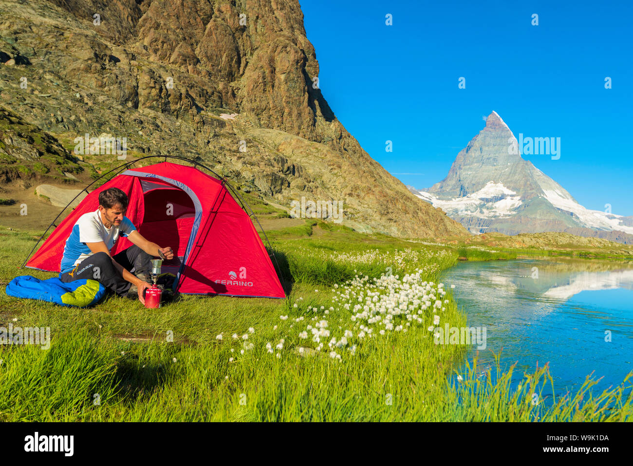 Hiker at lake Riffelsee makes coffee outside tent facing the Matterhorn, Zermatt, canton of Valais, Swiss Alps, Switzerland, Europe Stock Photo