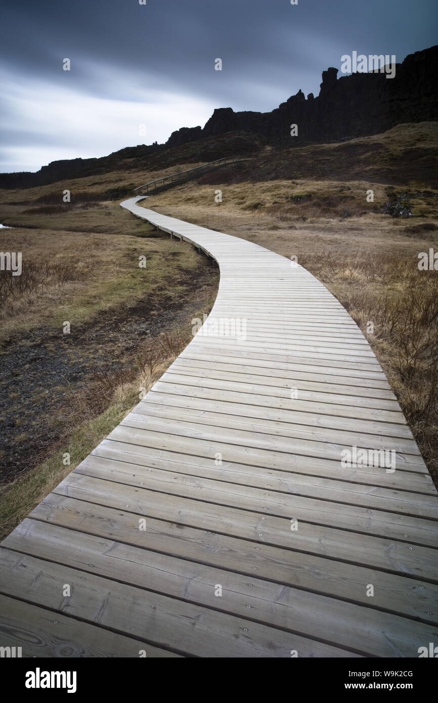 Boardwalk meandering towards rugged cliffs and stormy sky at Thingvellir National Park near Reykjavik, Iceland, Polar Regions Stock Photo