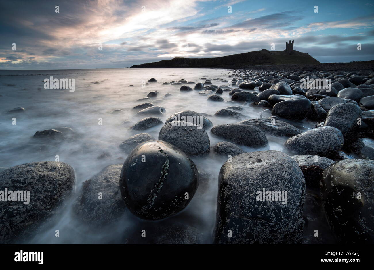 View at sunrise towards the ruin of Dunstanburgh Castle from The Rumble Churn at the Embleton Bay, Embleton, Northumberland, UK Stock Photo