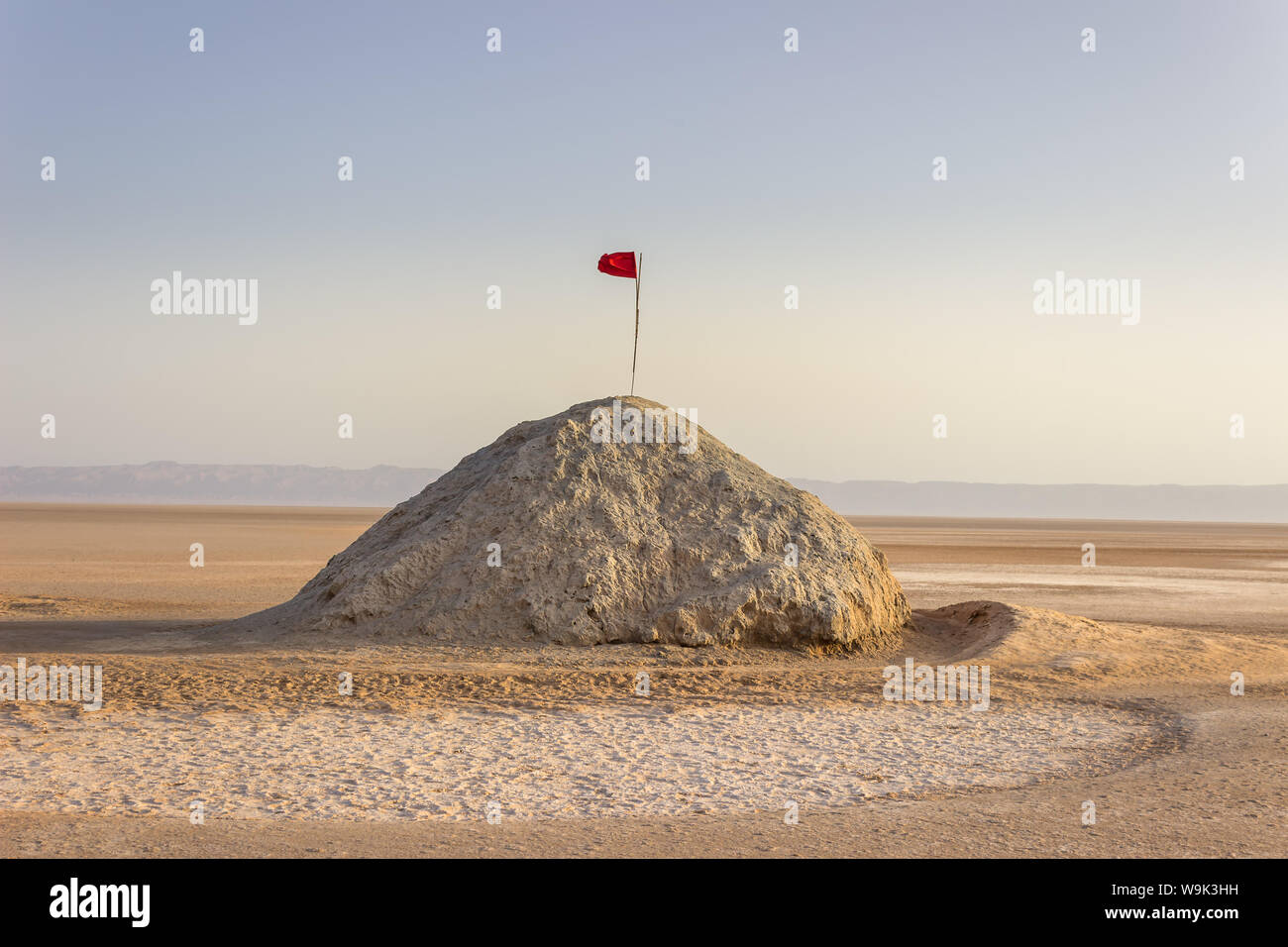 Chott el Djerid, the largest salt lake flats in Sahara desert in Tunisia and Tunisian red flag at the top of the hill under the blue sky Stock Photo