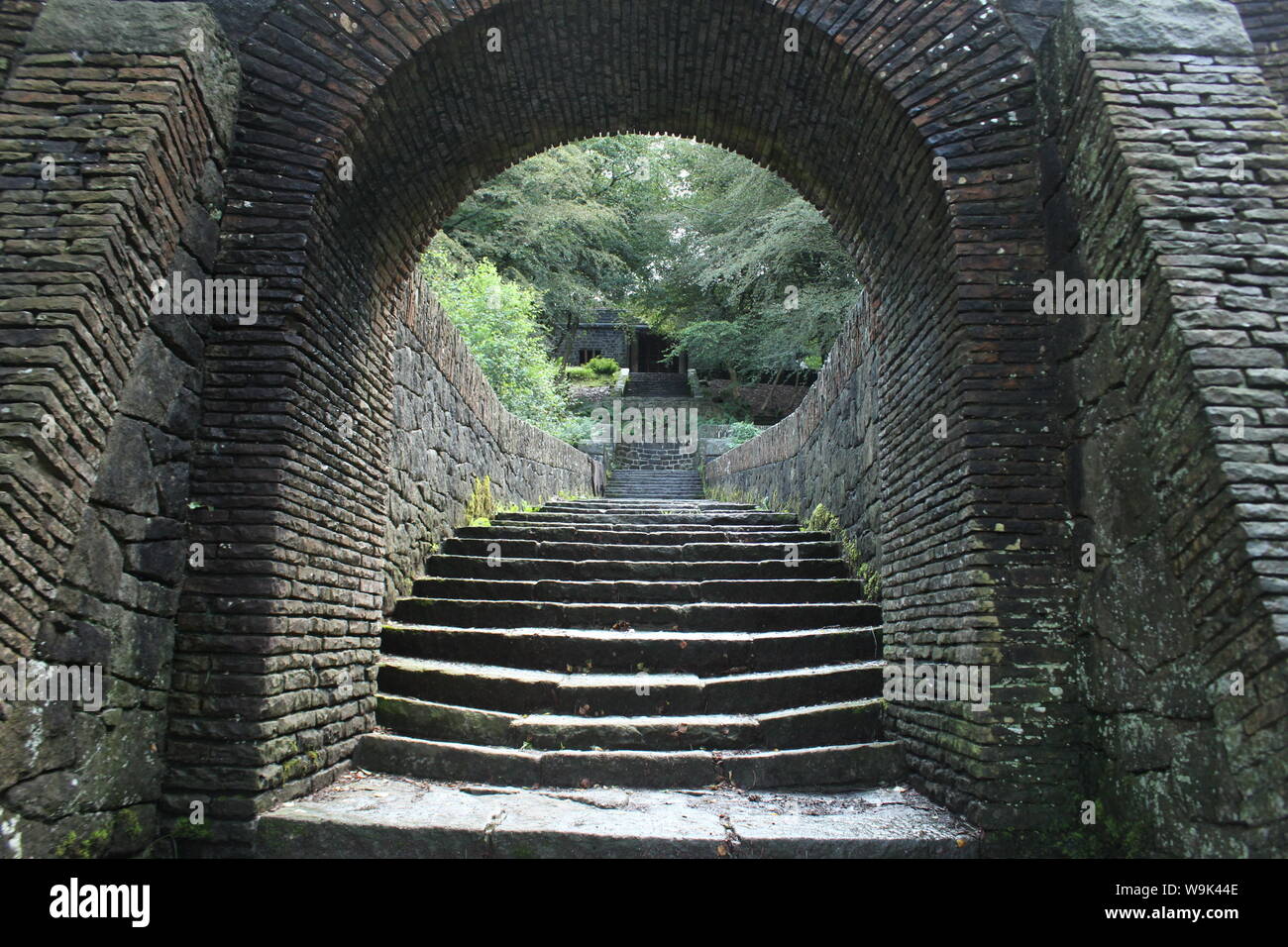 Image of an old stone tunnel arch and stairs in front of trees and a small building in Rivington Pike Stock Photo