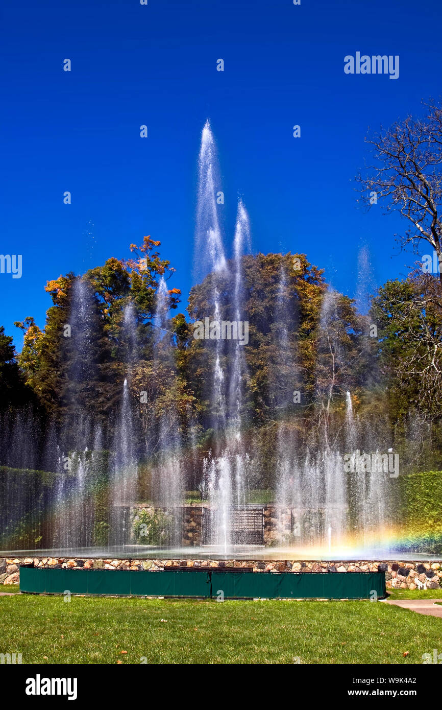fountains shooting water; varying heights; trees; rainbow, green grass