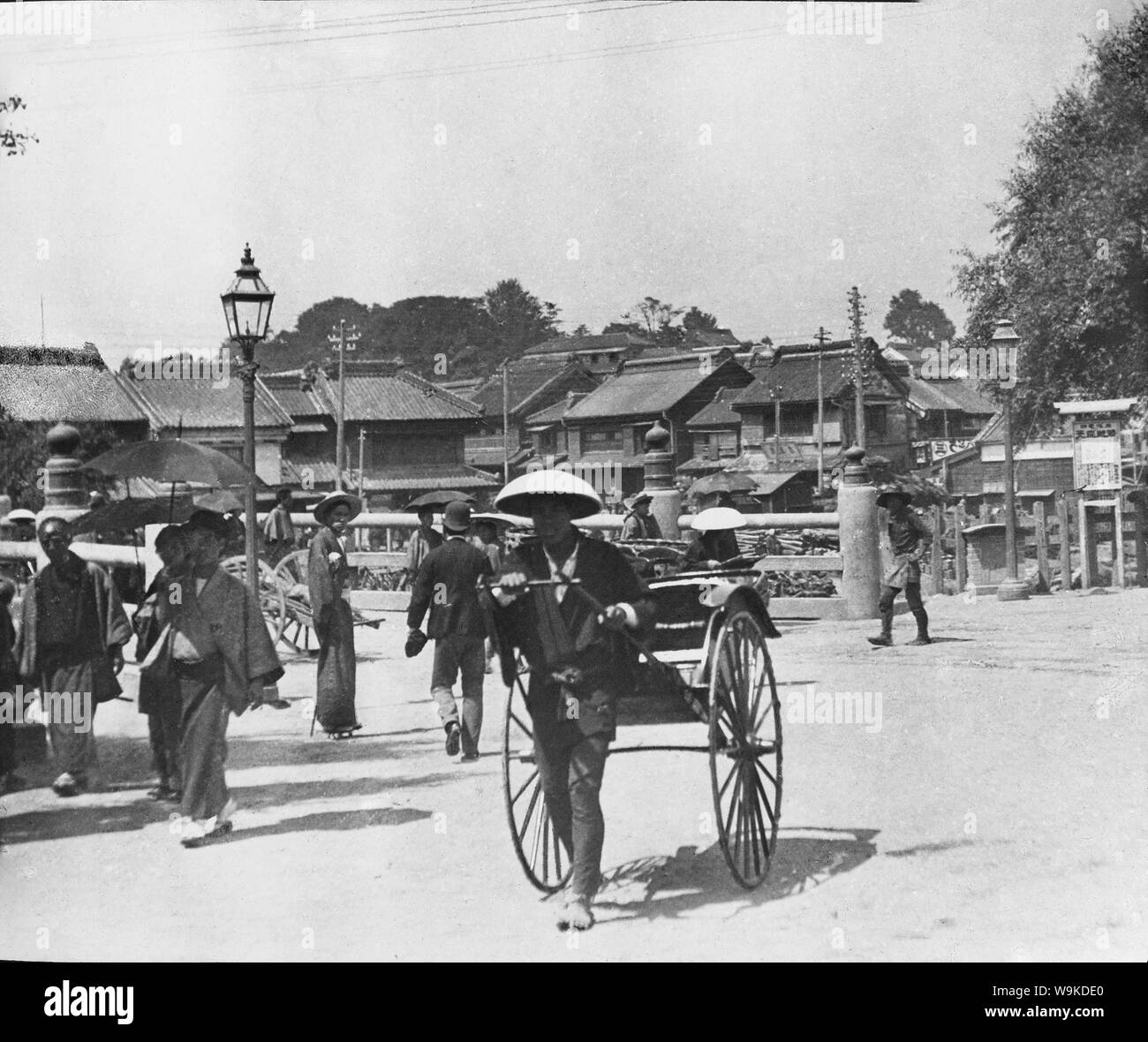 [ 1890s Japan - Japanese Rickshaw ] —   Rickshaw near bridge in an urban Japanese landscape.  From a series of glass slides published (but not photographed) by Scottish photographer George Washington Wilson (1823–1893). Wilson's firm was one of the largest publishers of photographic prints in the world.  19th century vintage glass slide. Stock Photo