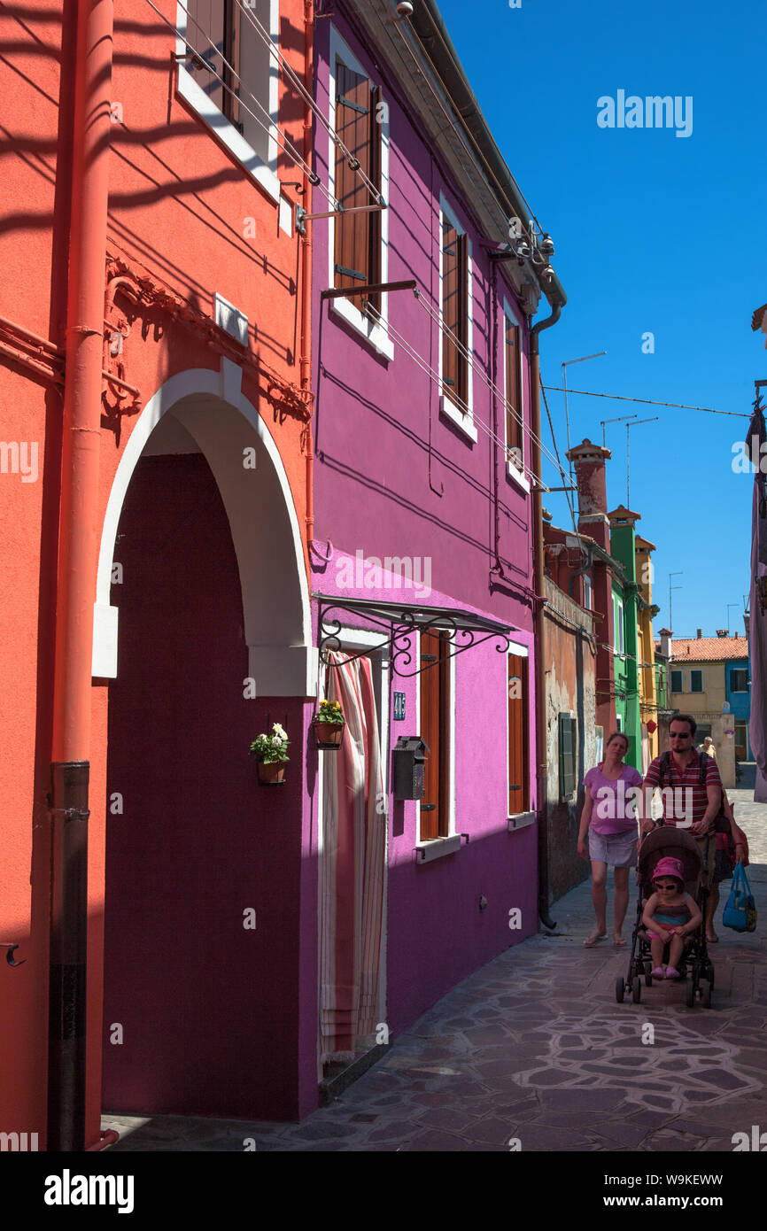 Family stroll past garishly painted houses in Corte del Pistor, Burano Stock Photo