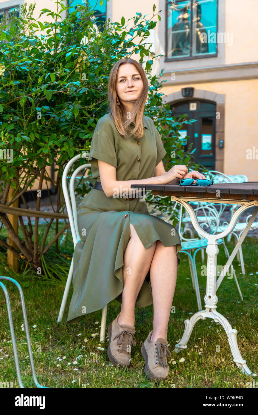 Blonde young girl in a summer dress sits and rests in a street cafe on a sunny summer day. Tourism concept Stock Photo