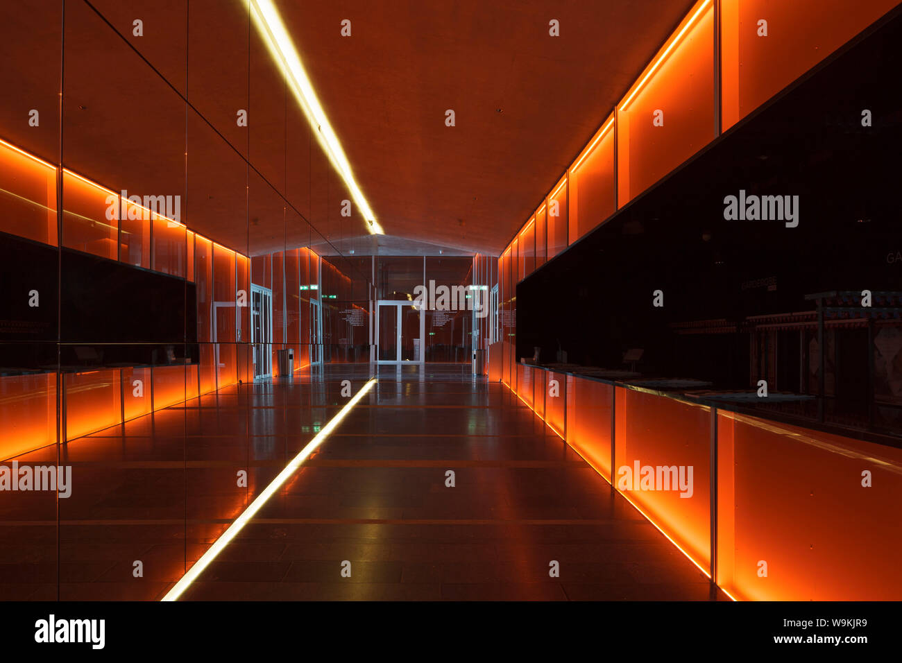 Orange-lit corridor on ground floor, with cloakroom to right. DE KOM Theatre, Nieuwegein, Netherlands. Architect: de Architekten Cie, 2012. Stock Photo