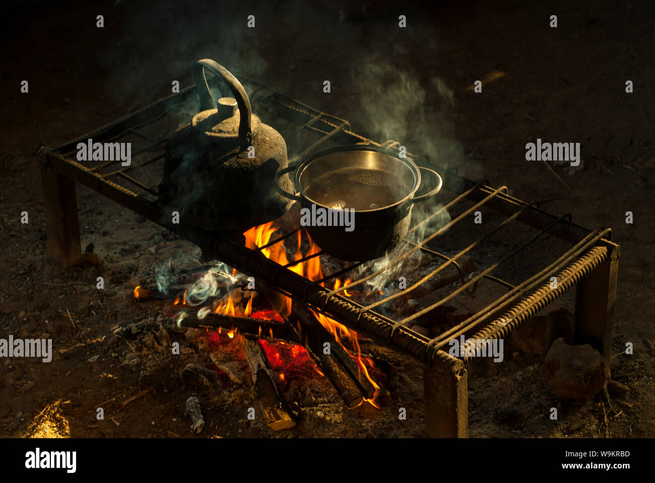 a pot and a kettle stand over a fire on a portable hearth made of metal