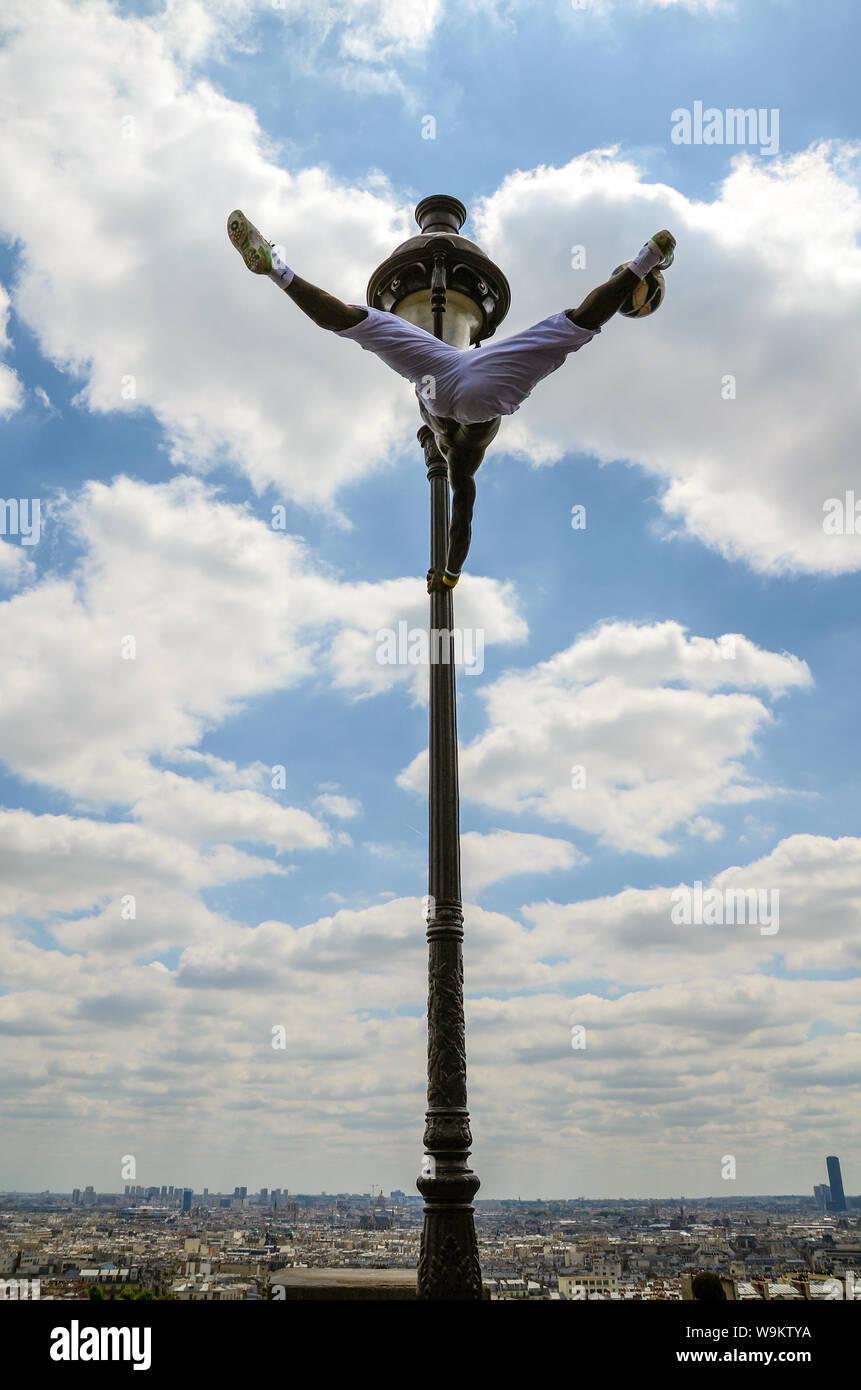 Street performer in Paris, France, performing on a lamp post at Sacré-Cœur overlooking the city. Football skills and acrobatic athleticism. Skyline Stock Photo