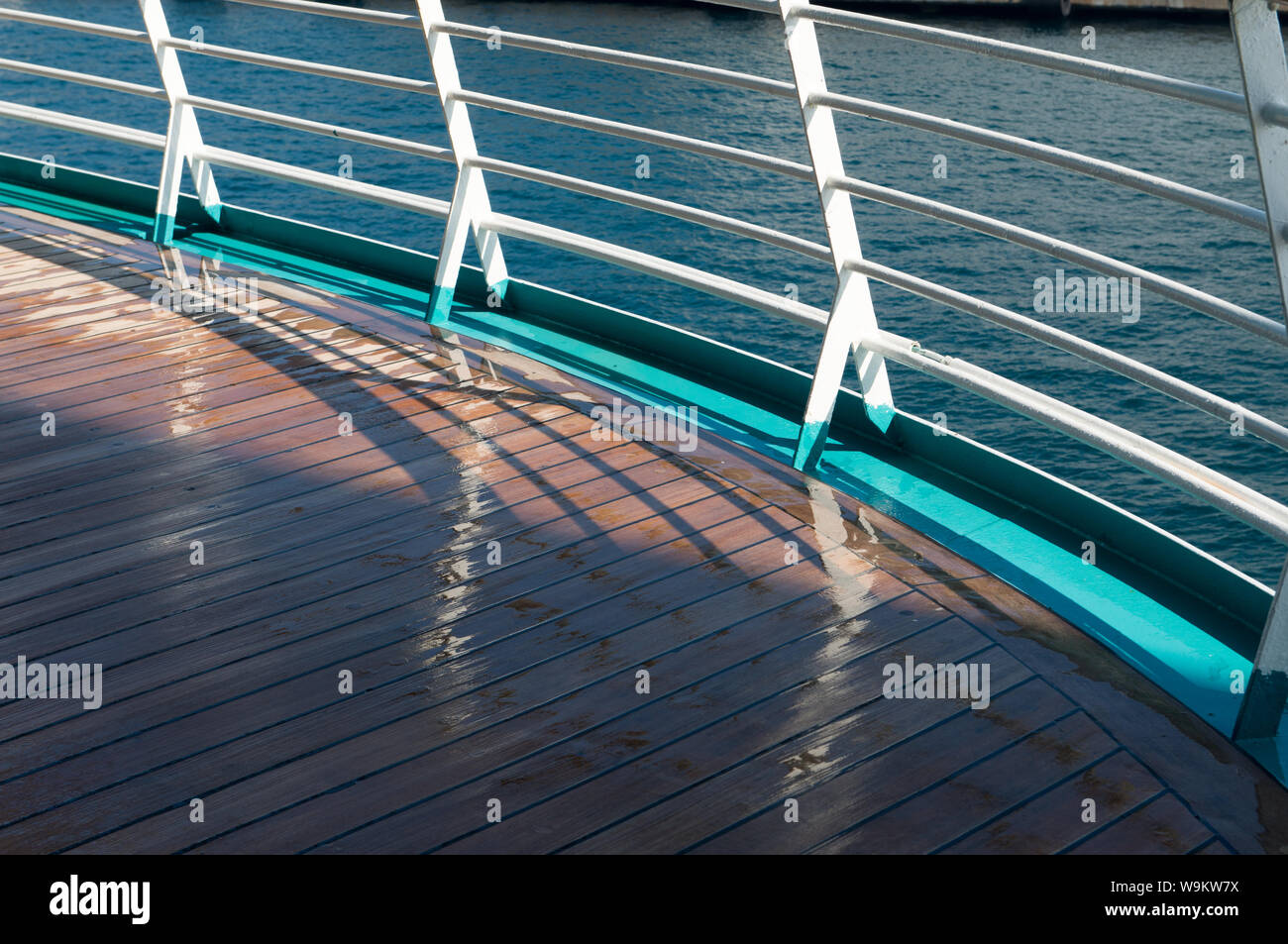 Curved metal safety rail with wet wooden decking on nautical vessal ...