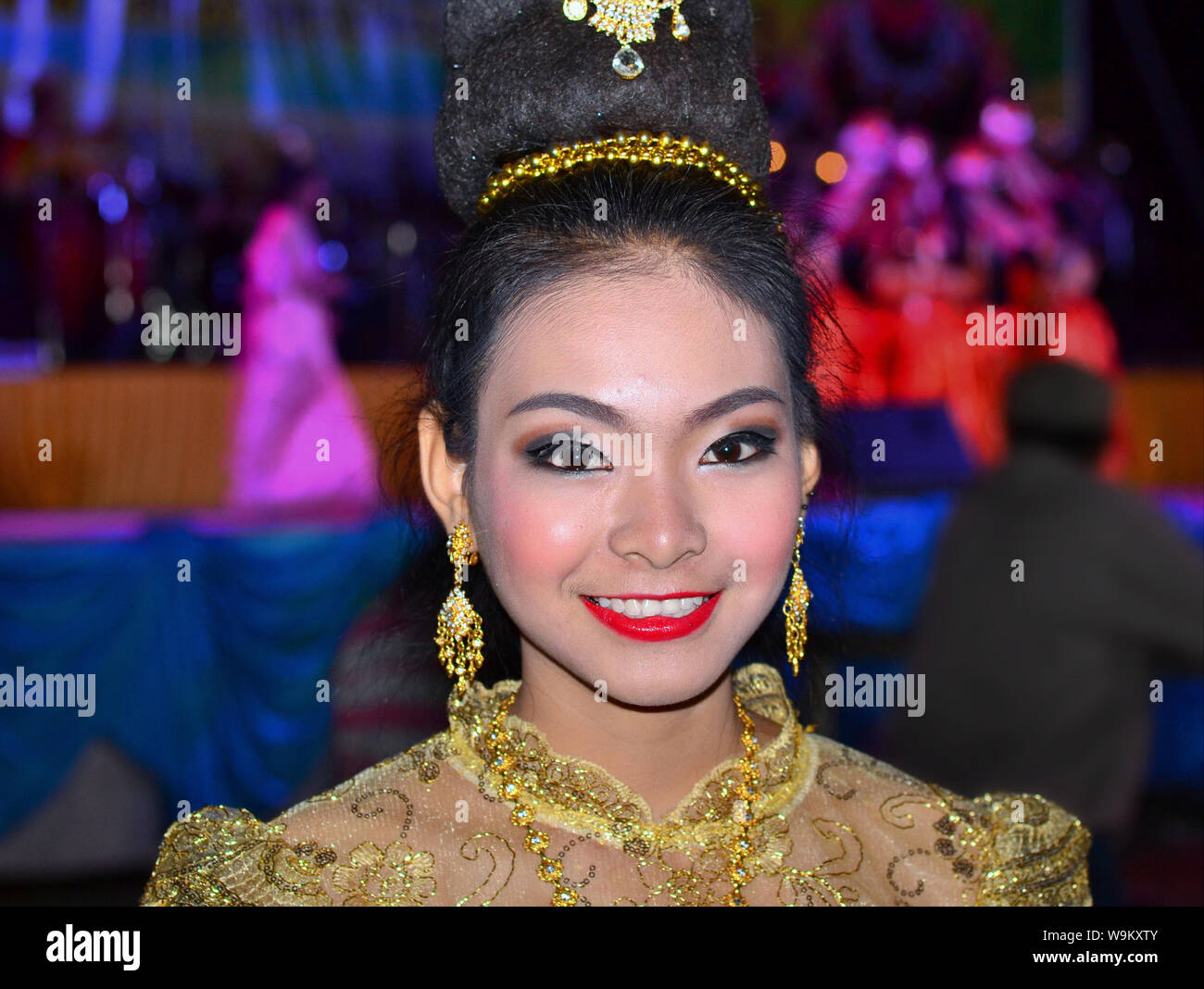 Dressed-up Thai girl wears a golden Lanna-style lace dress and elaborate hairdo with hair jewellery and drop earrings during a rural Yi Peng parade. Stock Photo