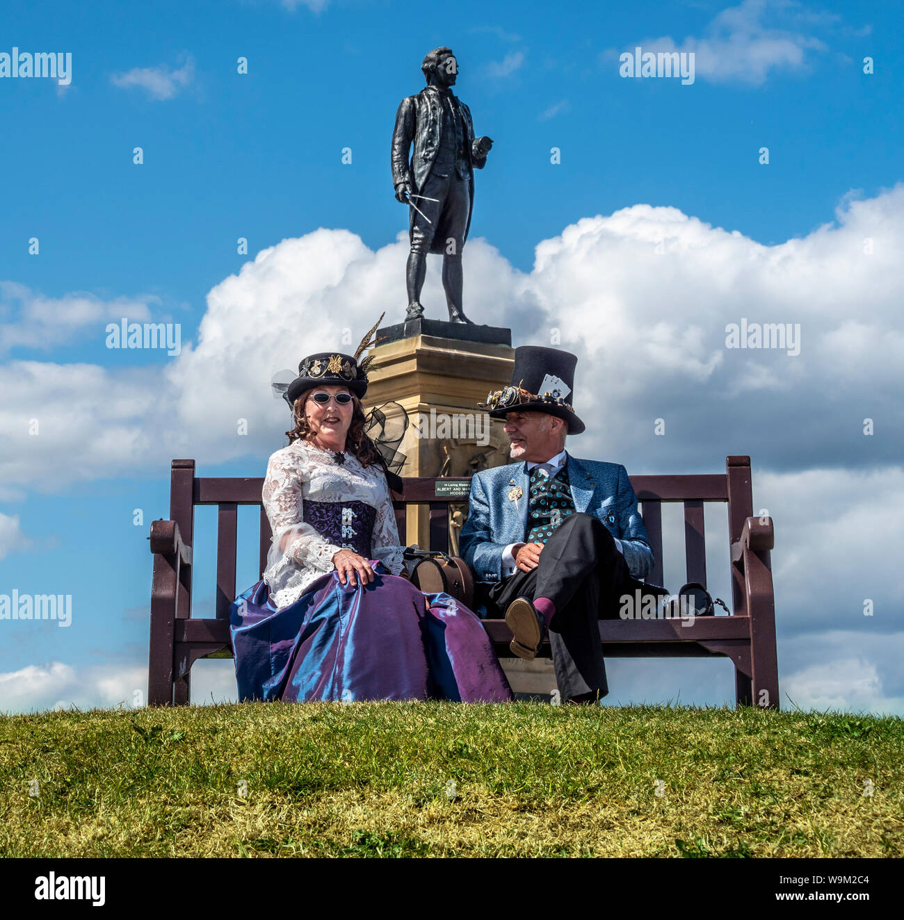 Steampunk couple sat on bench below Captain Cook memorial, Whitby, UK. Stock Photo