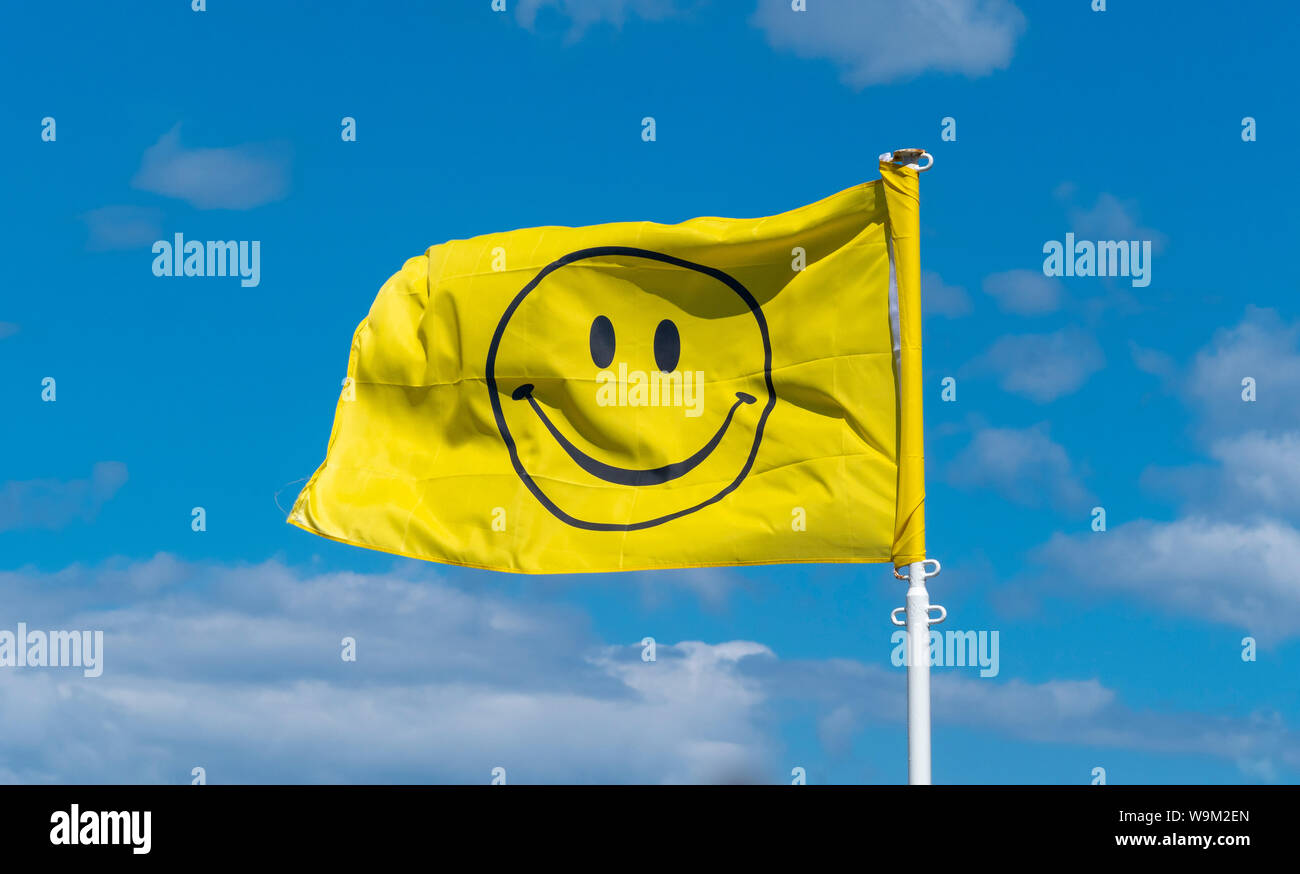 Smiley face symbol on yellow flag against blue sky Stock Photo