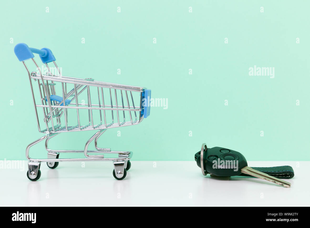 Car purchase concept. Empty shopping cart and car keys on white table with light blue background Stock Photo