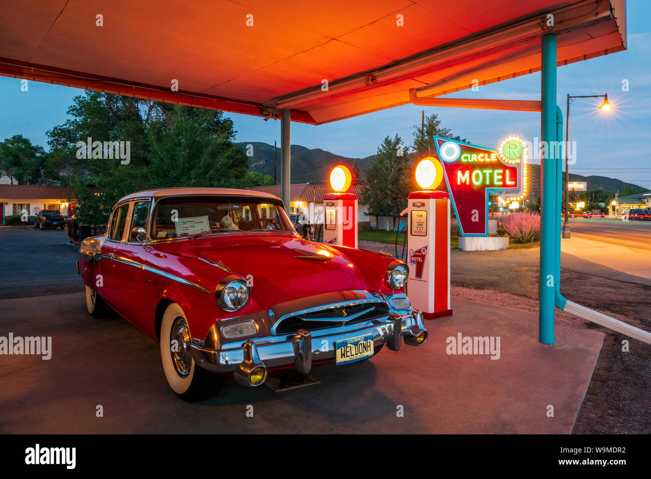 Dusk view of 1955 Studebaker President classic car parked in front of antique gas pumps converted to electric car chargers; The Circle R Motel; Salida Stock Photo