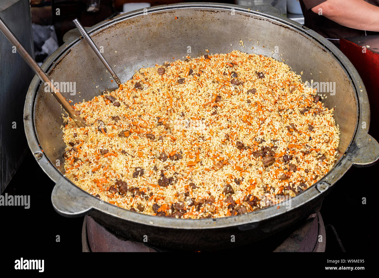 Cooking of traditional pilaf in big cauldron on food market, national