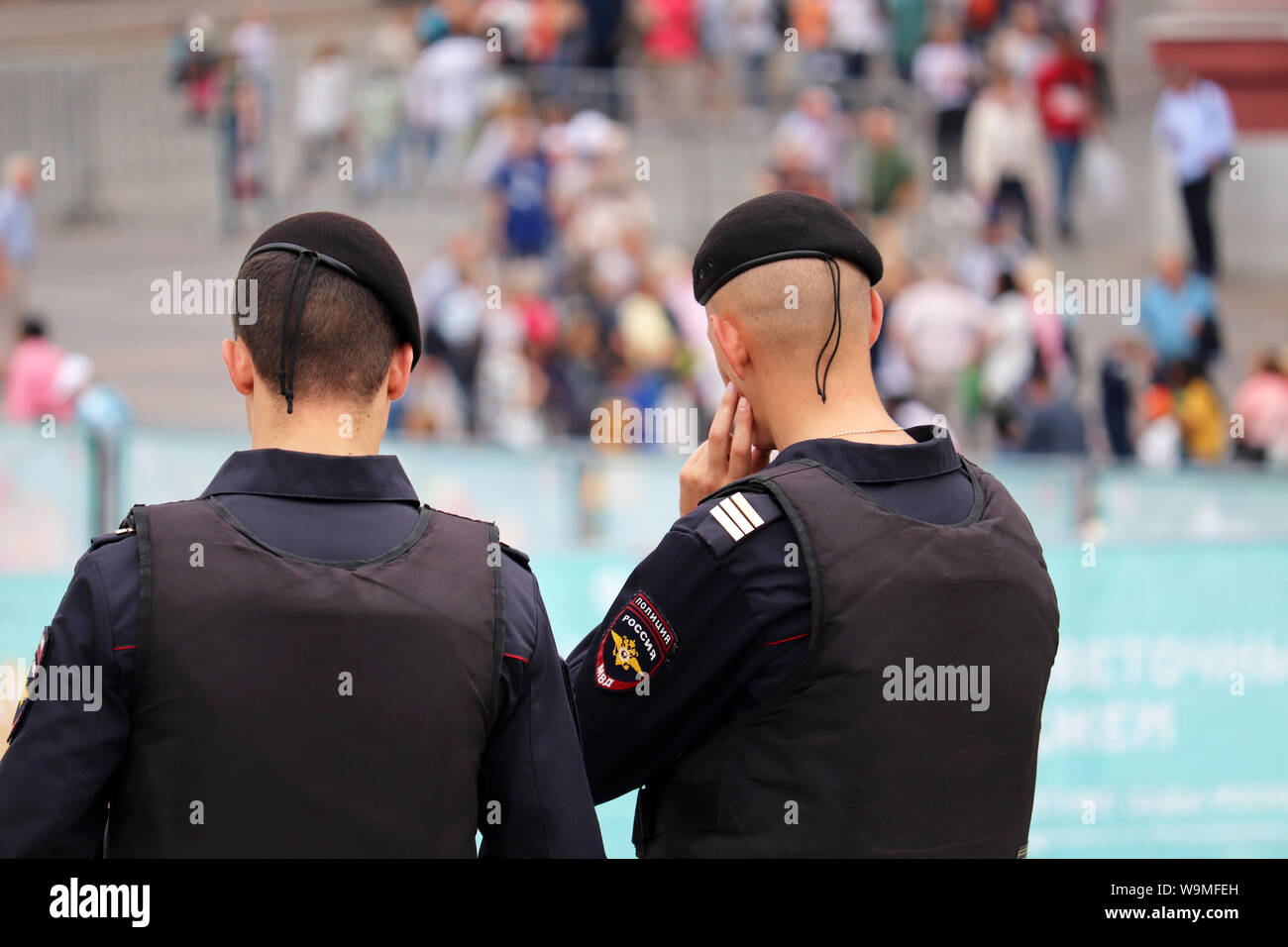 Two russian police officers stand on background of a crowd of people, street patrol. Law enforcement agencies, concept of law and order Stock Photo