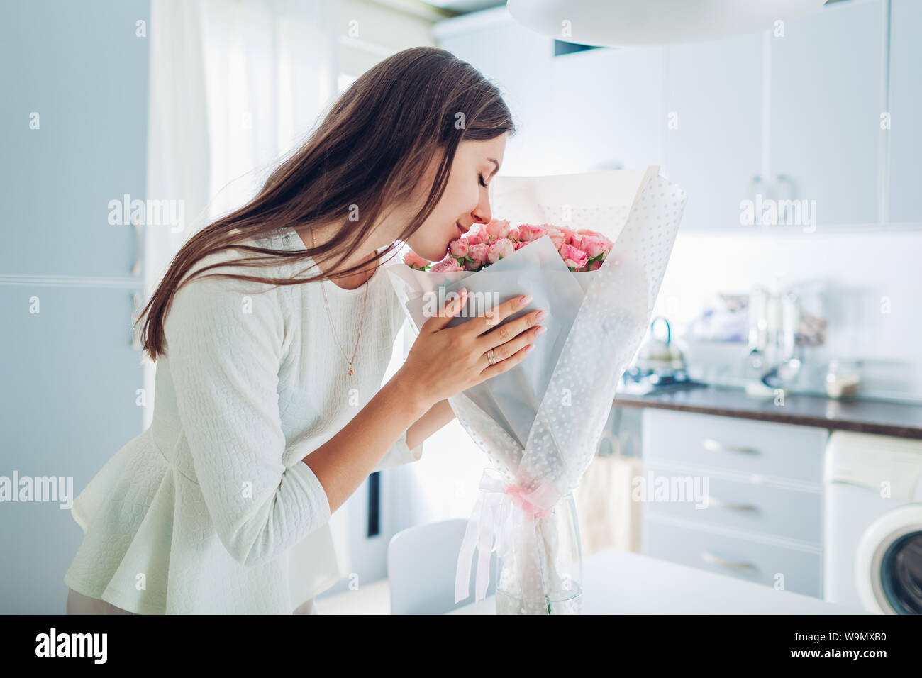 Happy woman smelling bouquet of roses. Housewife enjoying decor and interior of kitchen. Sweet home. Allergy free Stock Photo