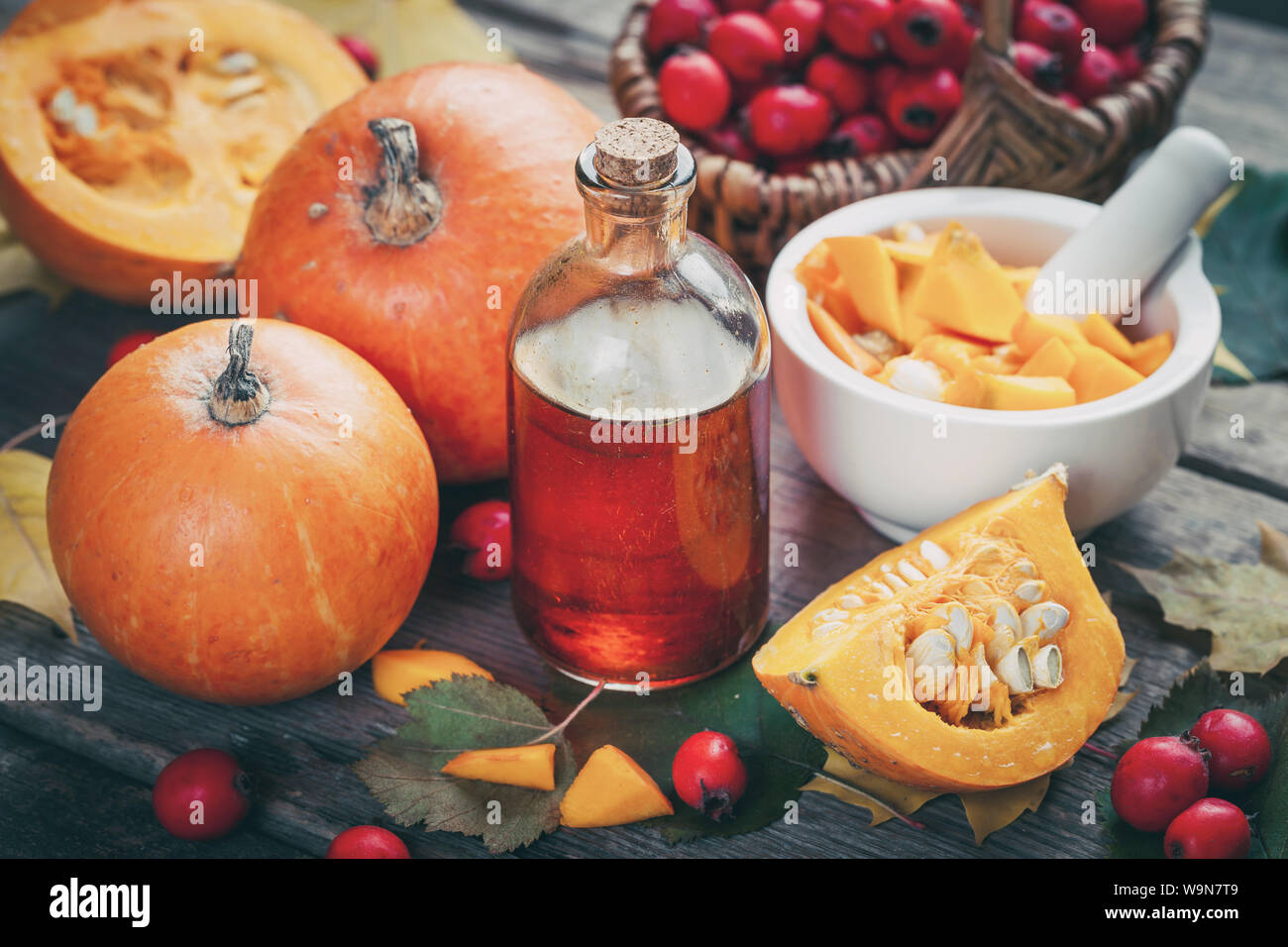 Pumpkin seeds oil bottle, pumpkins, mortar and basket of  hawthorn berries on wooden table with autumn leaves. Stock Photo