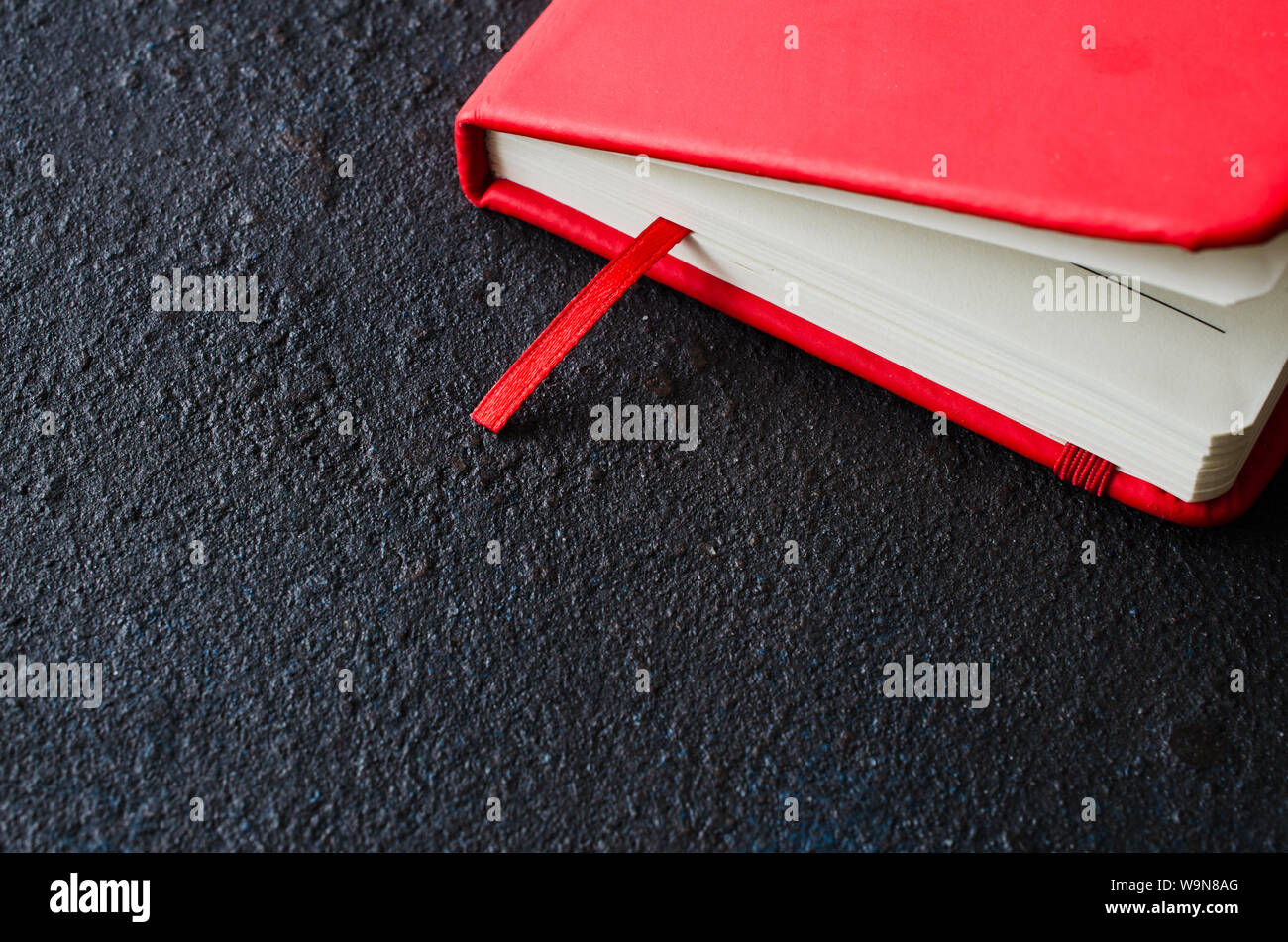 Red closed notebook for writing or book on dark background. Stock Photo