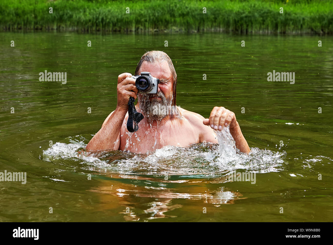 Wet mature bearded man is standing in water and taking pictures by digital camera. Stock Photo