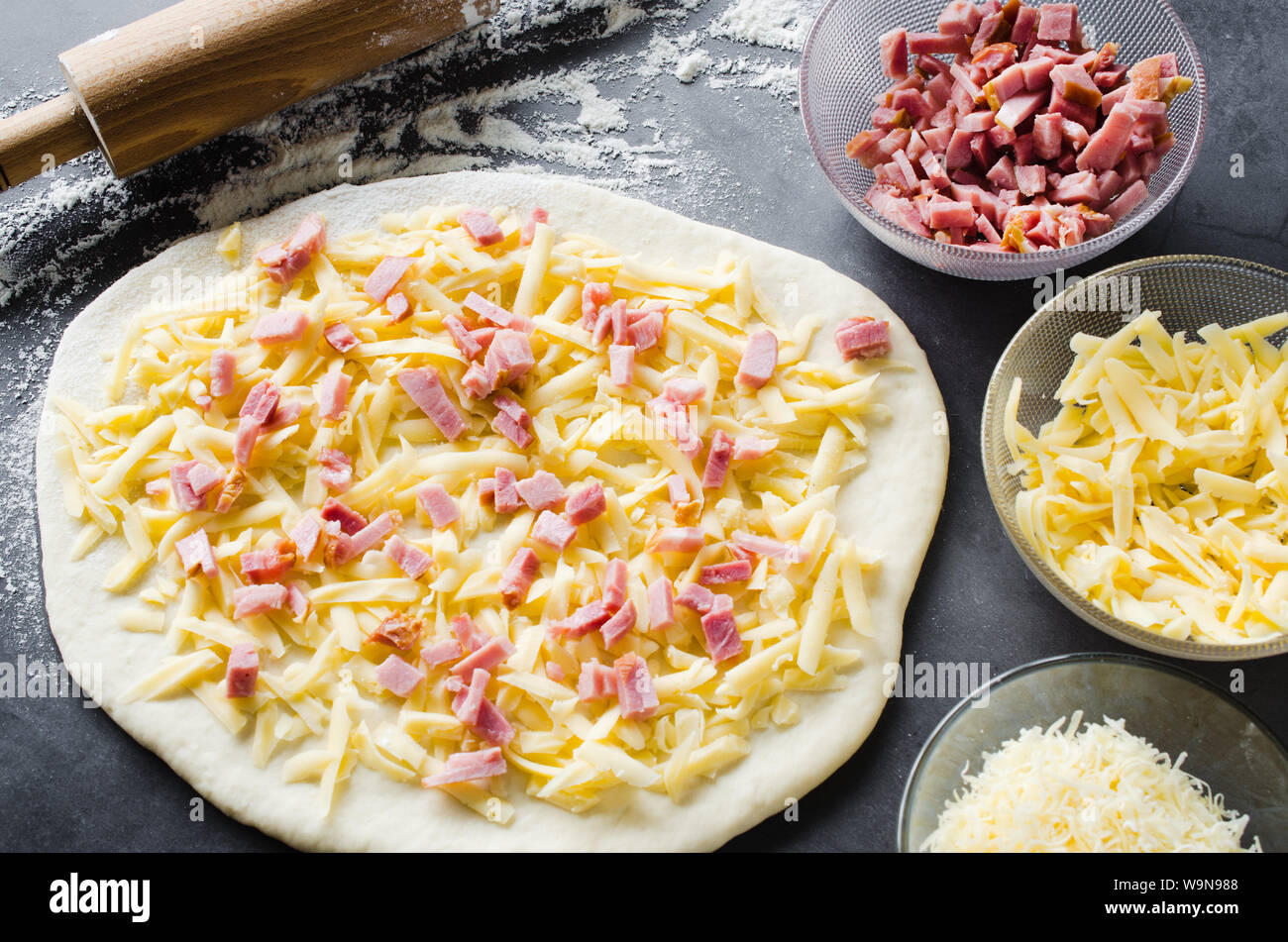 Rolled dough, baking flour, pizza filling and rolling pin on a dark