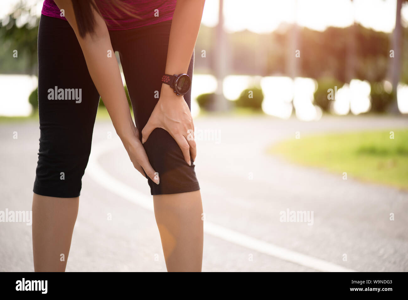 Young fitness woman runner feel pain on her knee in the park. Outdoor