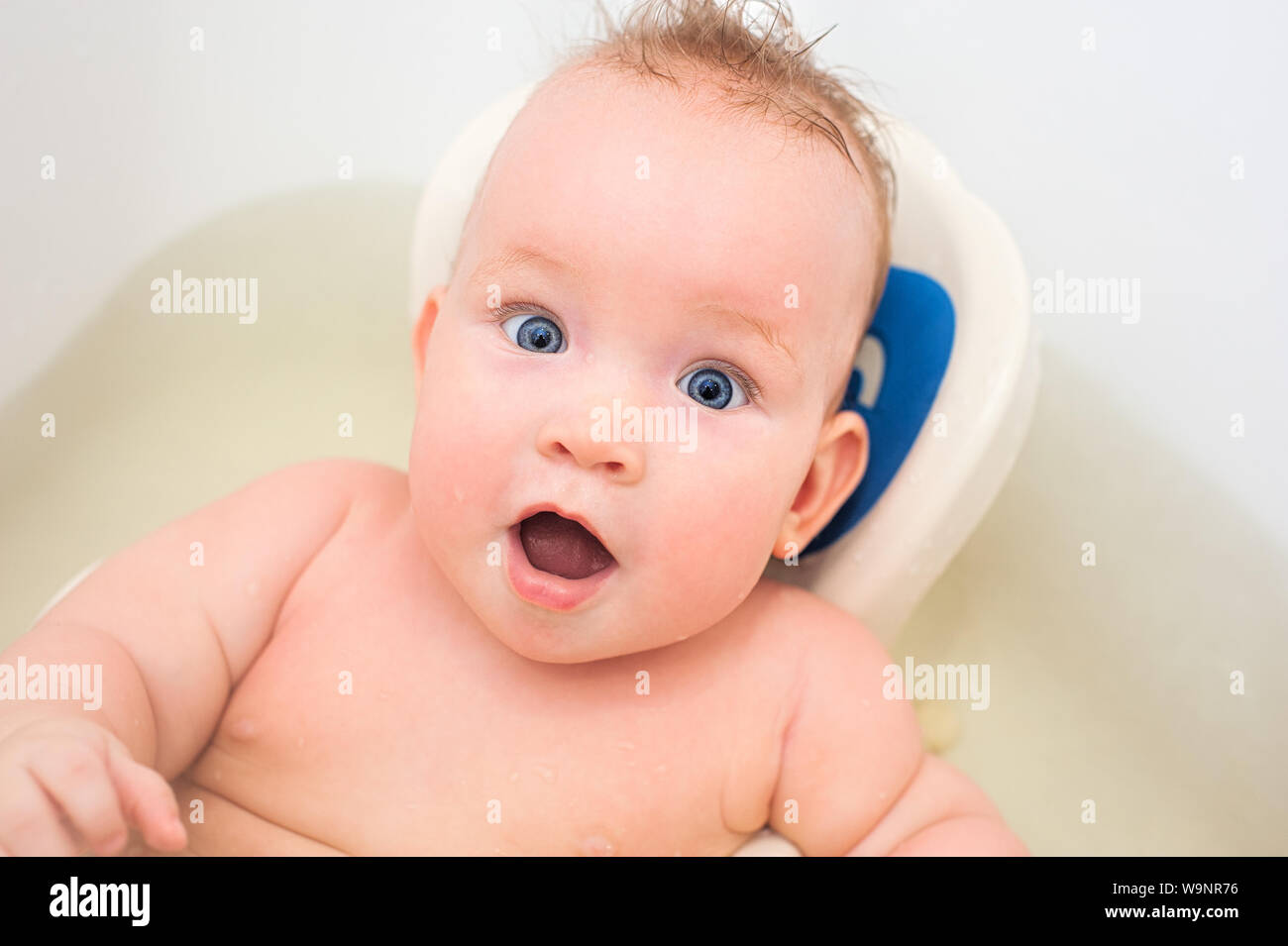 Surprised little baby swimming in the bath. American child bathroom surprised for game design. Pure water. Curly hair. Funny kid. Open mouth. Stock Photo